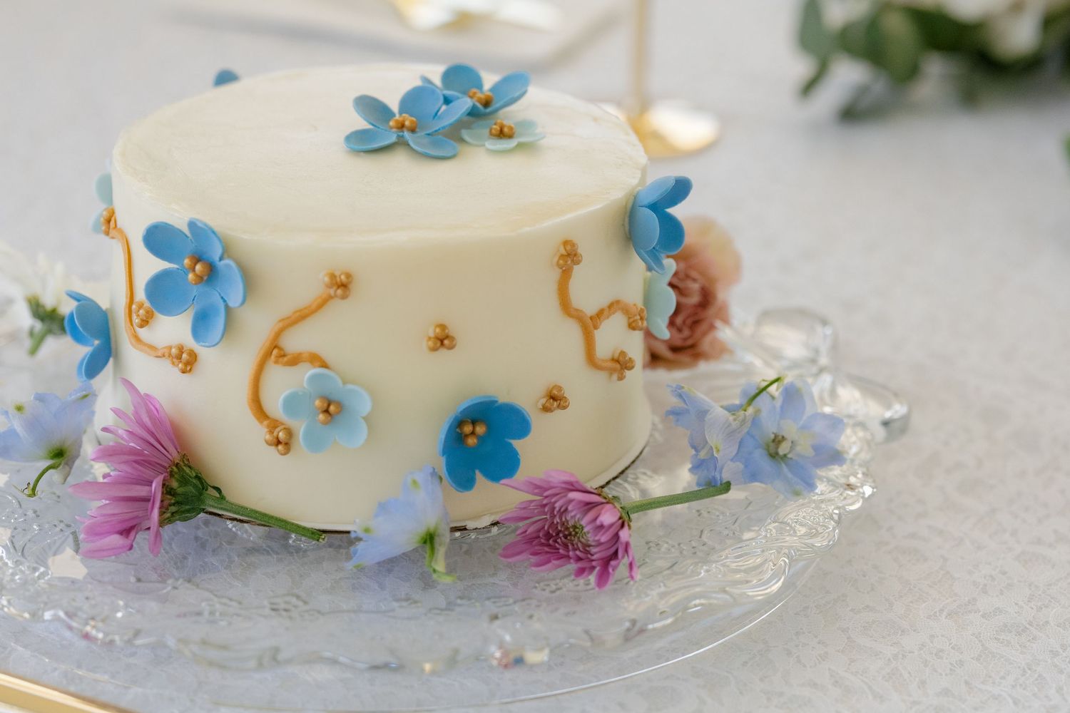 Wedding cake decorated with delicate blue flowers and pink blossoms on a crystal cake stand.