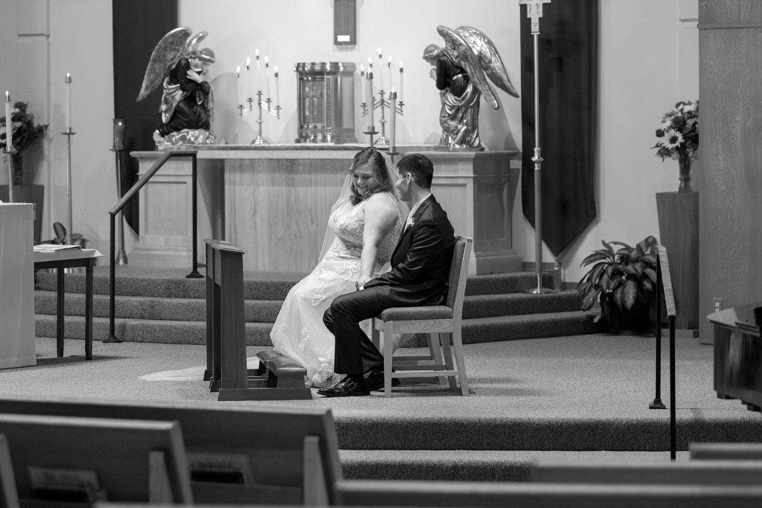 Black and white photo of wedding ceremony in traditional church setting with dramatic lighting.