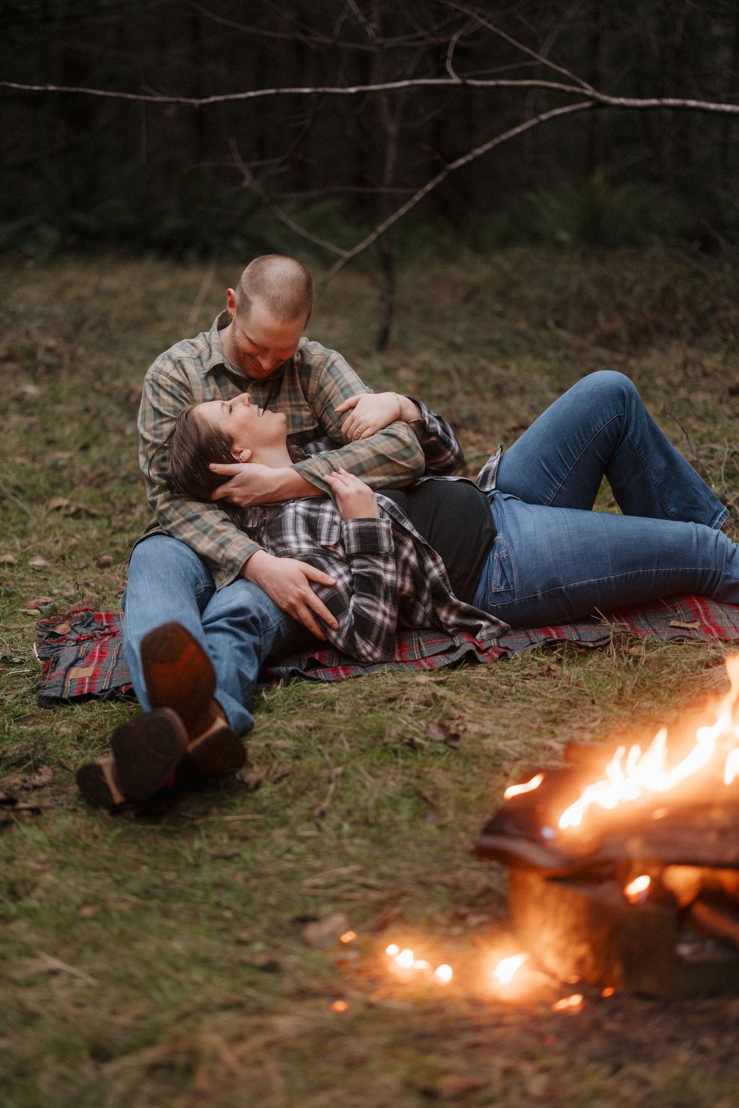 Intimate couple resting on ground with warm campfire flames in foreground.