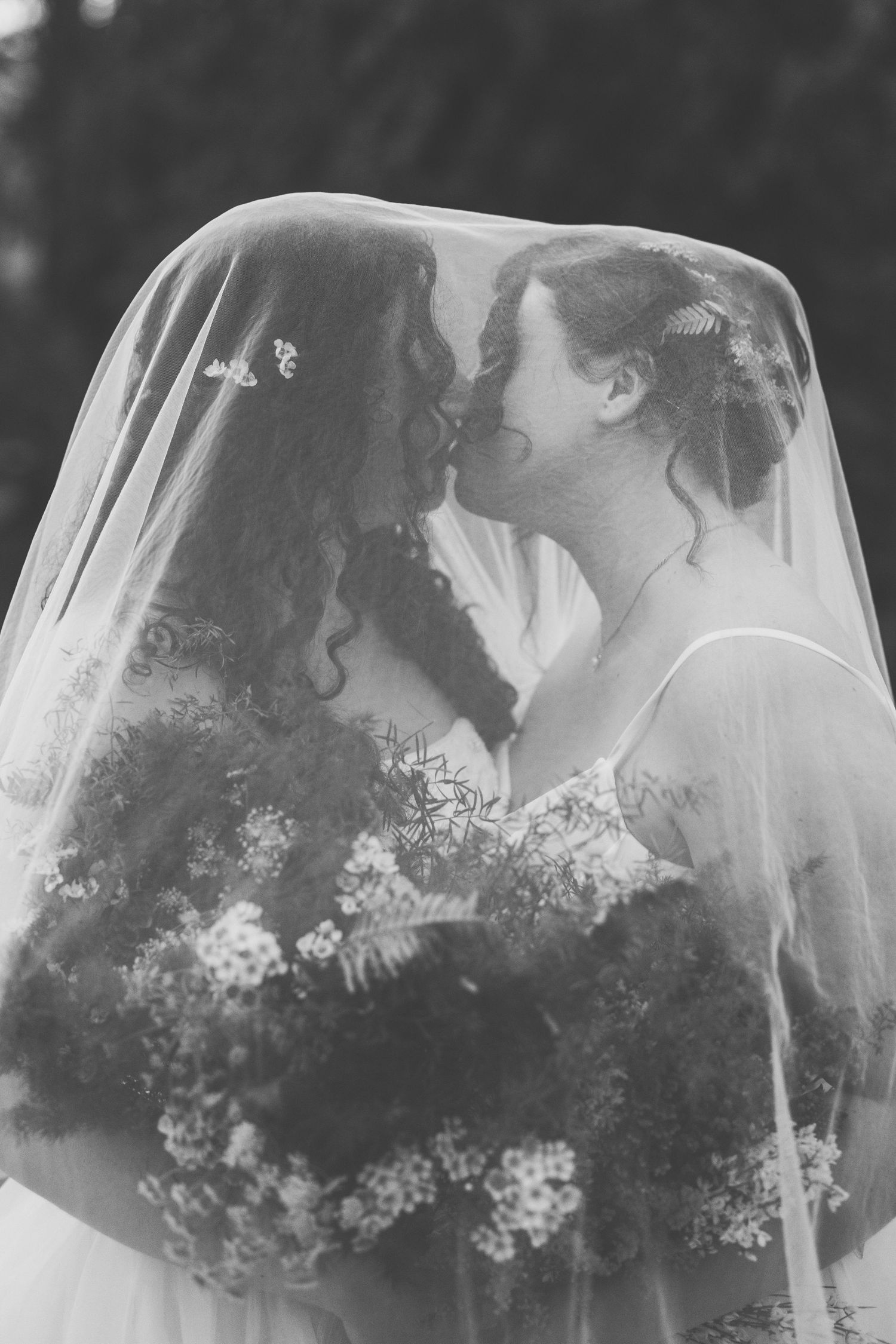 A romantic black and white wedding photo series showing a couple kissing under a delicate white veil with flowers.