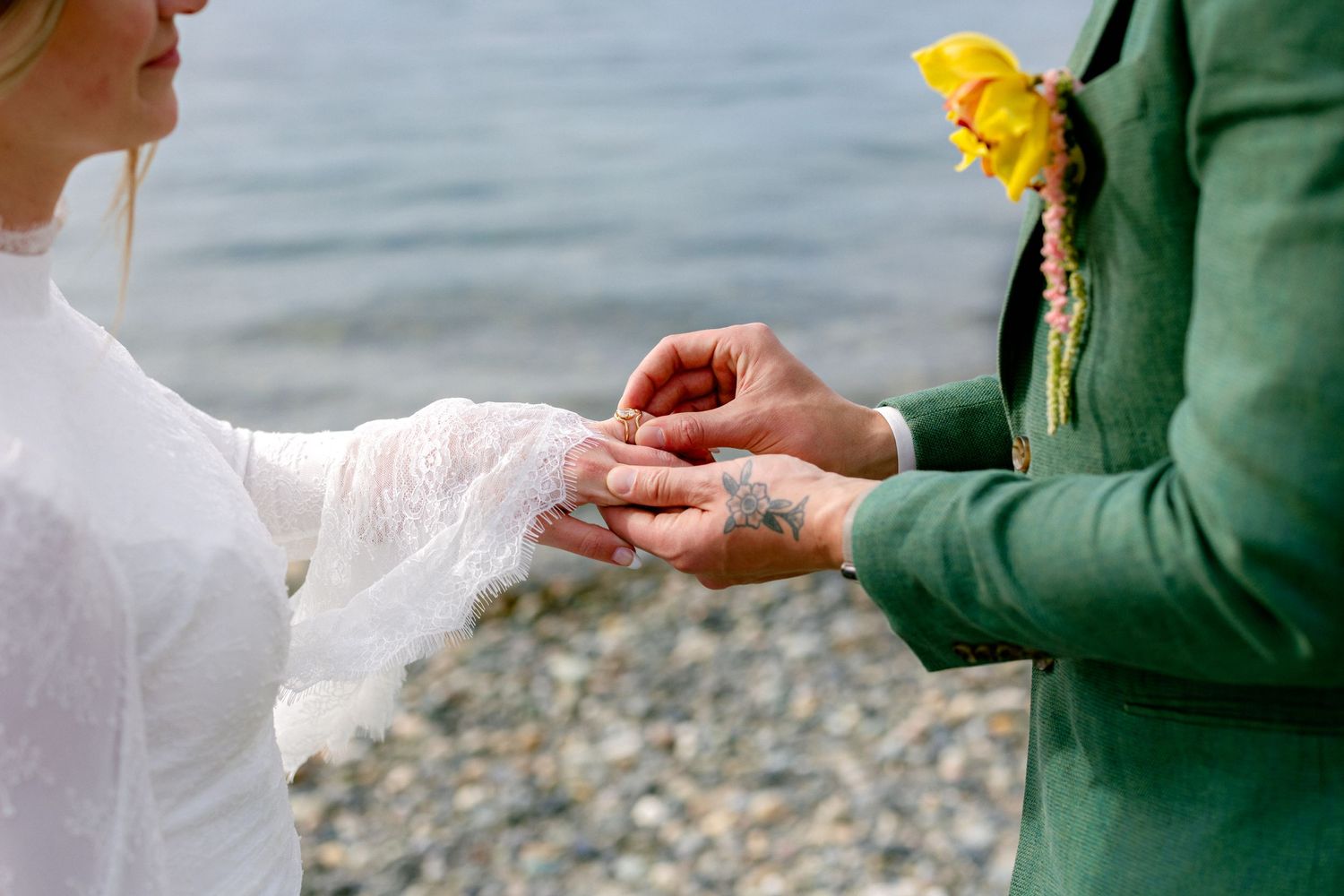 Bride and groom exchange rings on a rocky beach with ocean water in the background.