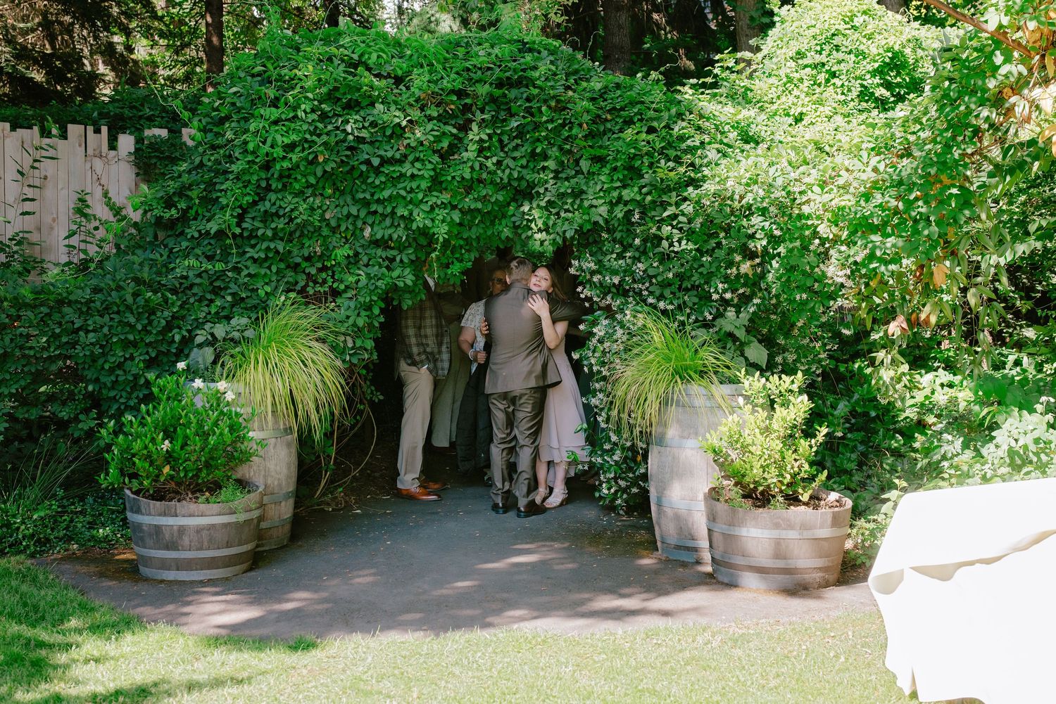 Guests entering lush green garden archway entrance at outdoor wedding venue.