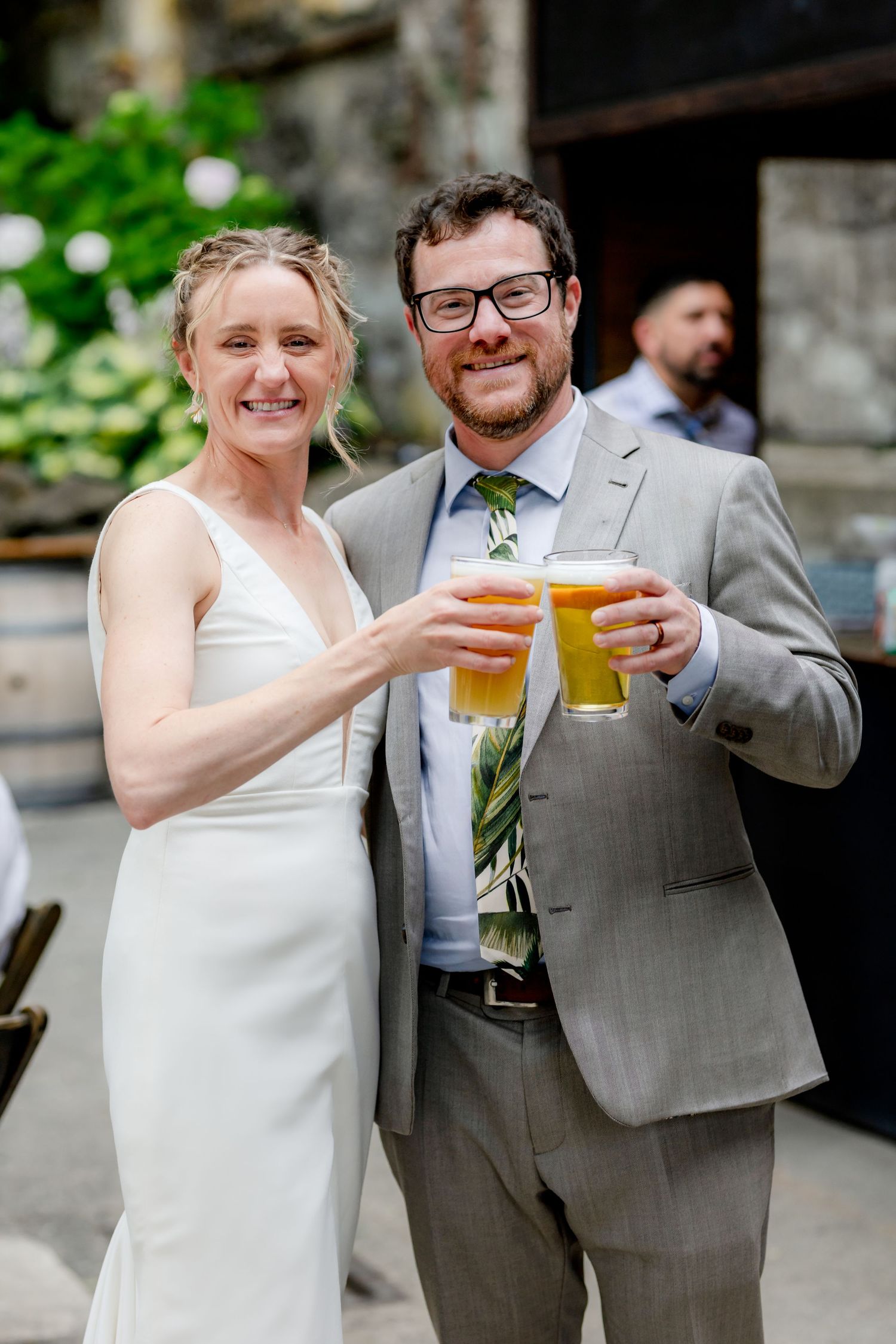 Bride and groom smiling and toasting with beer glasses at their outdoor wedding reception.