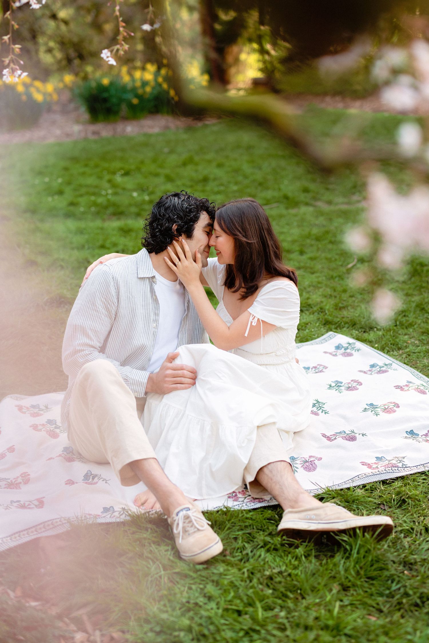 A couple shares an intimate moment on a picnic blanket under blooming spring trees.