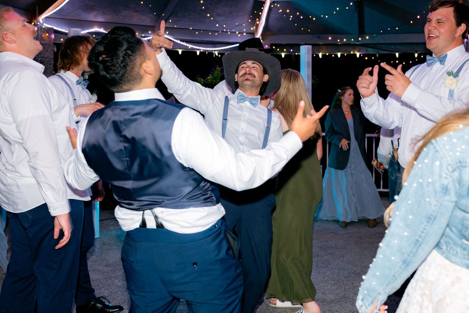 Guests dance and celebrate joyfully at an outdoor evening wedding reception under string lights.