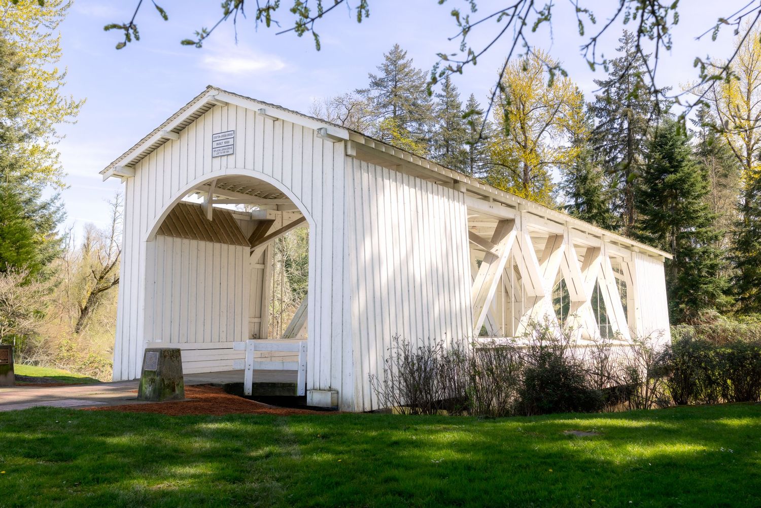 White covered bridge surrounded by lush green trees and grass on a sunny day.