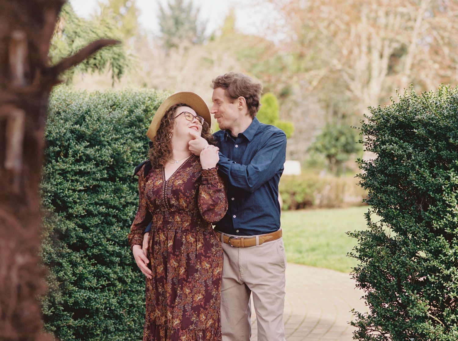 A romantic couple shares tender moments together while walking through a lush garden pathway on a sunny afternoon.