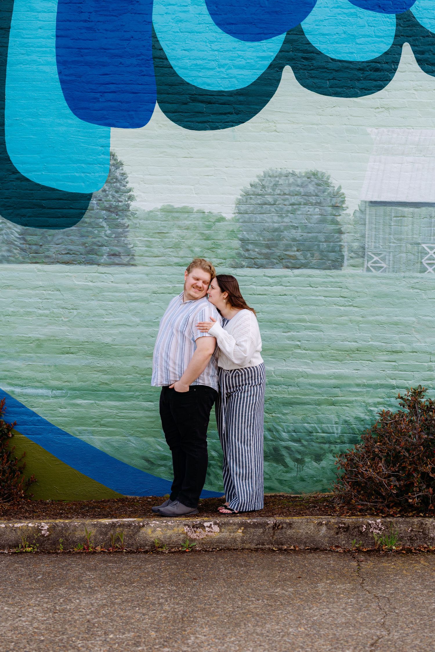 A couple embraces near a vibrant blue painted wall mural outdoors.
