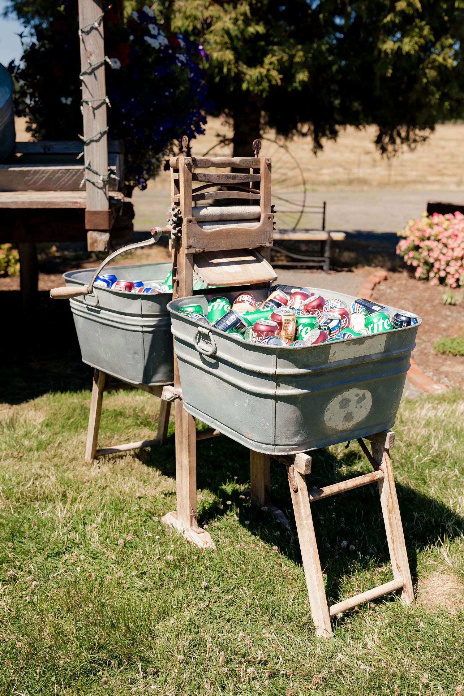 Two galvanized metal tubs filled with ice and canned beverages on rustic wooden stands outdoors.