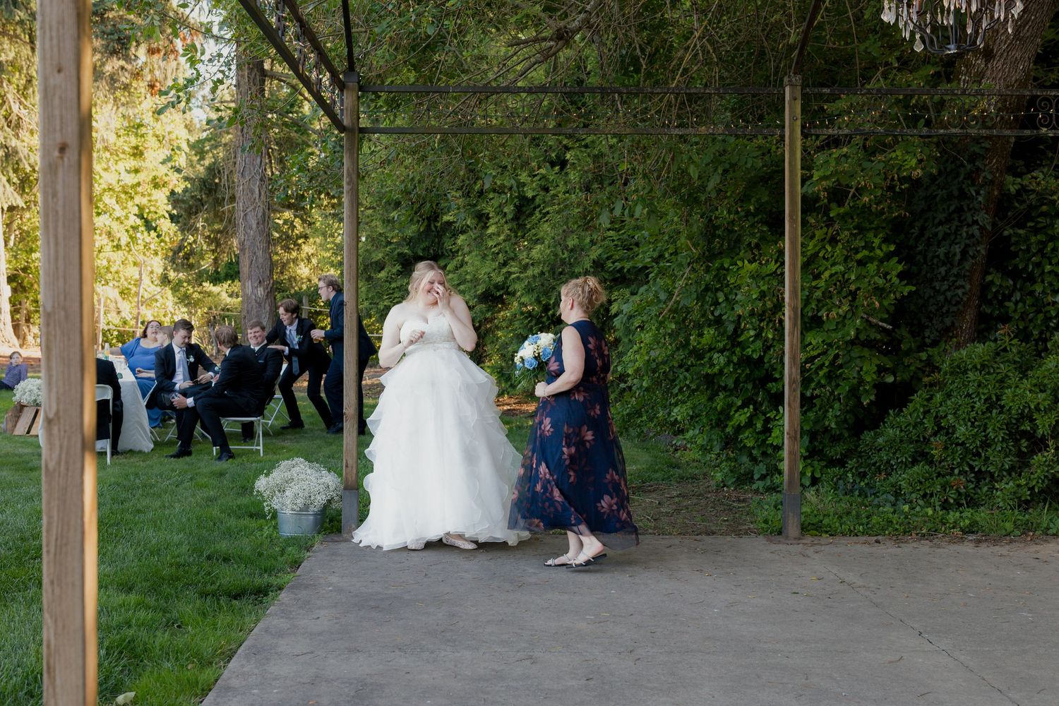 Bride in white gown walks with bridesmaid toward an outdoor wedding venue.
