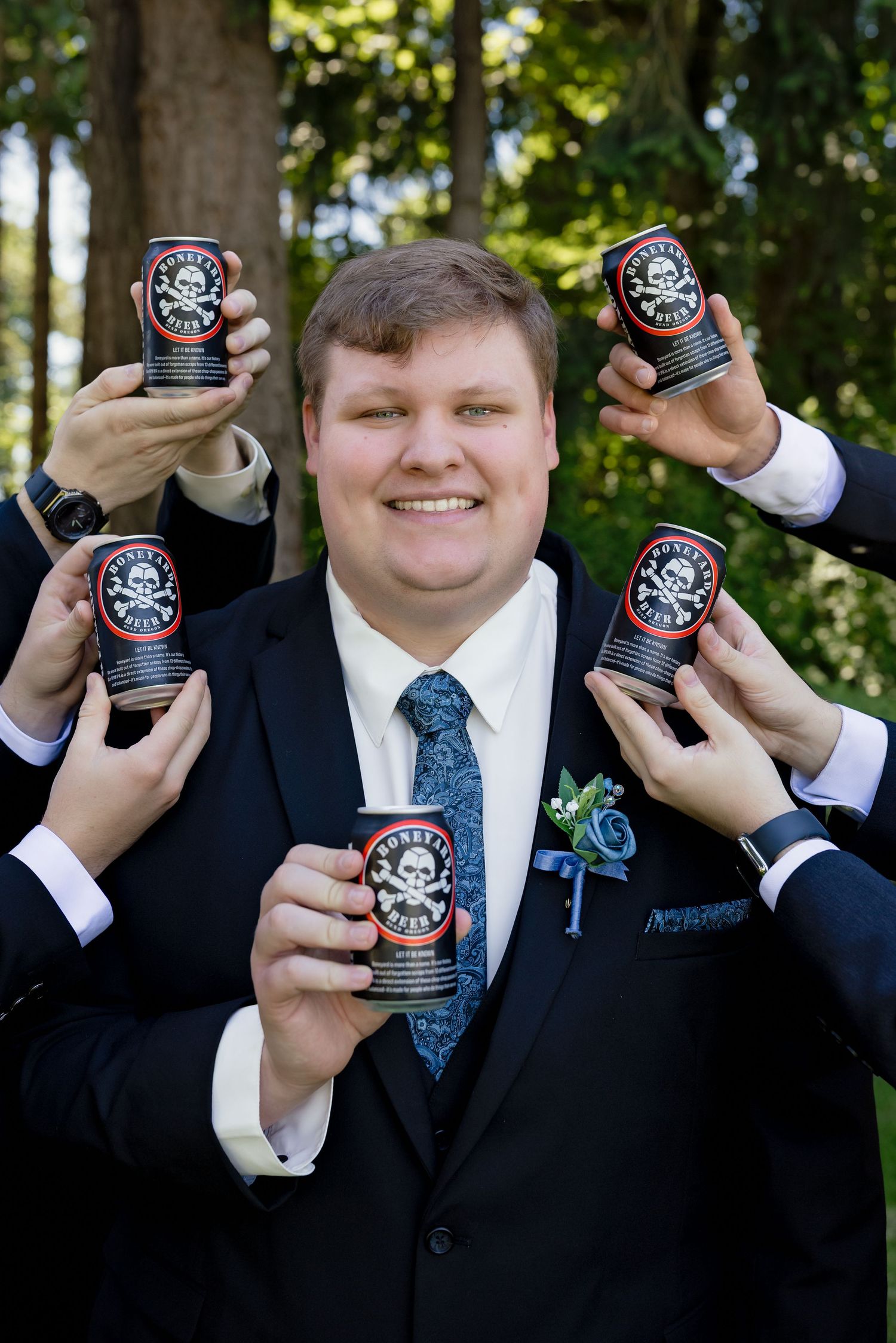 Smiling groom in navy suit holding beer can surrounded by groomsmen also holding cans.