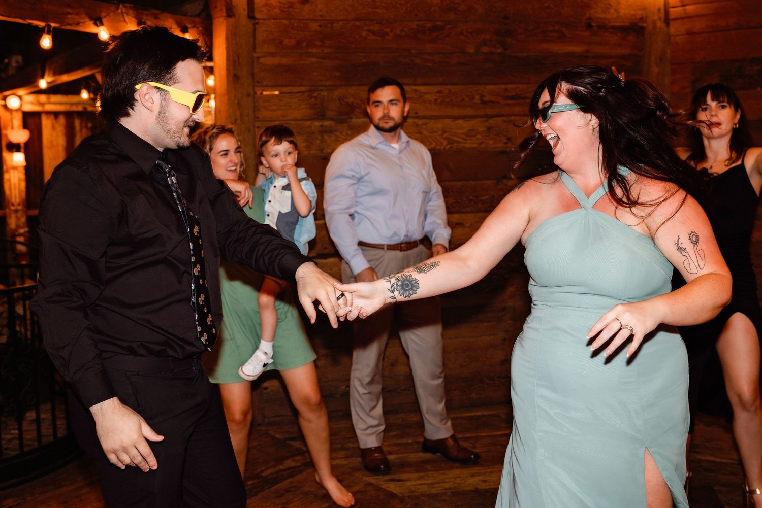 Couple dancing together at a wedding reception in a rustic barn venue with guests watching in the background.