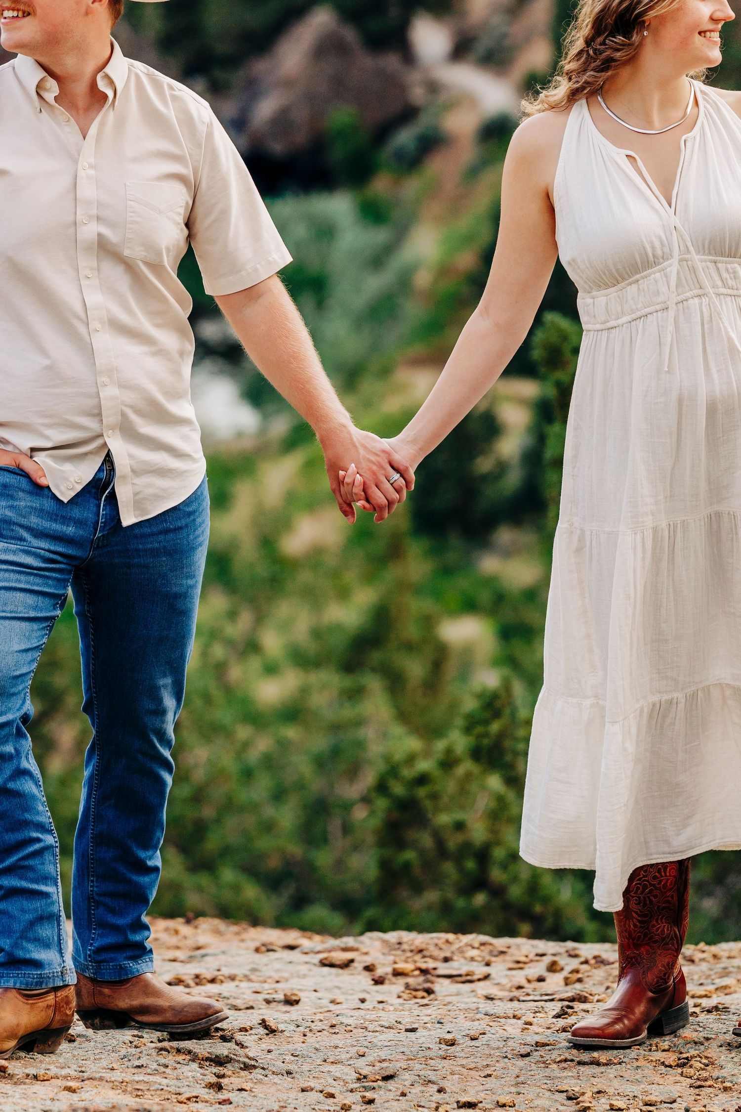 A couple in western attire holding hands while standing on a dirt path outdoors.