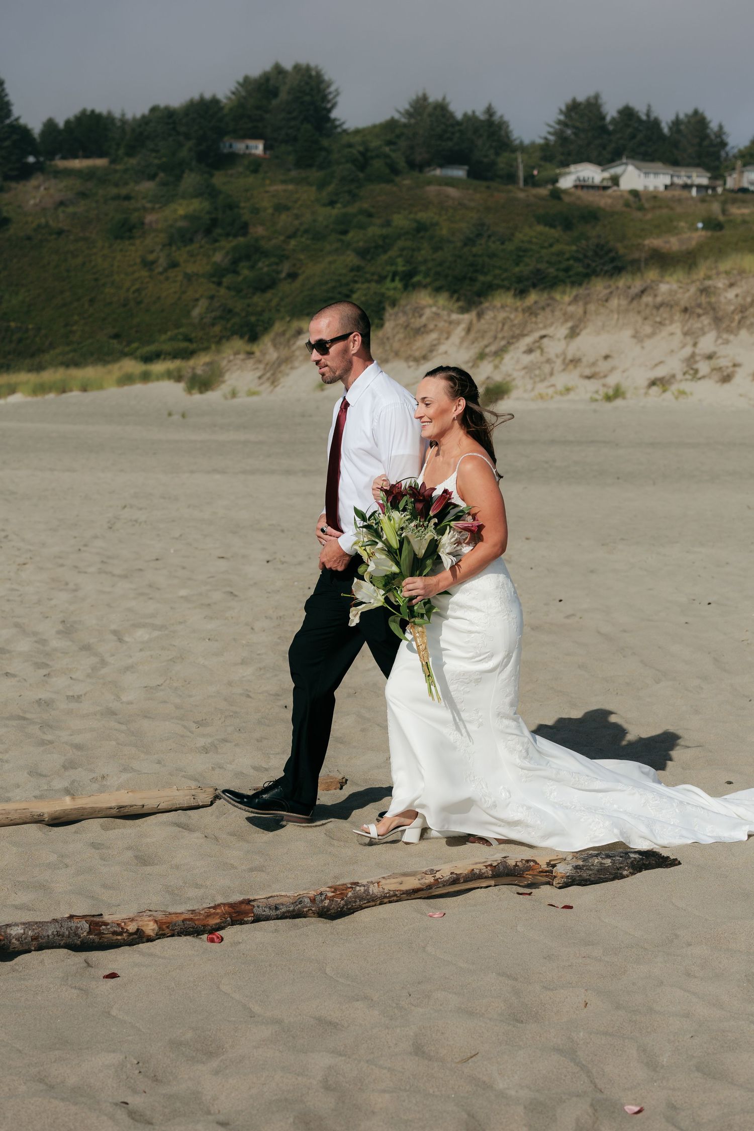 A beach wedding photo of a couple walking on driftwood with coastal cliffs in the background.