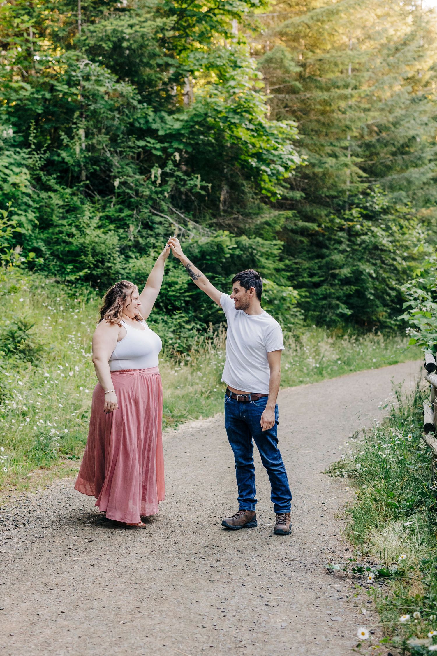 A couple dances playfully on a forest path surrounded by summer greenery and wildflowers.