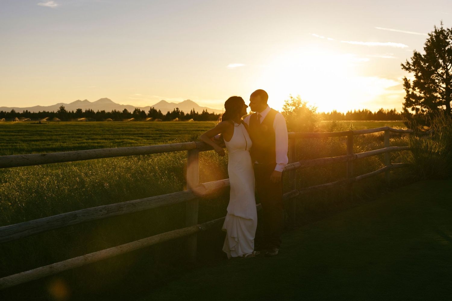 Silhouettes stand against a dramatic sunset sky over rural farmland.