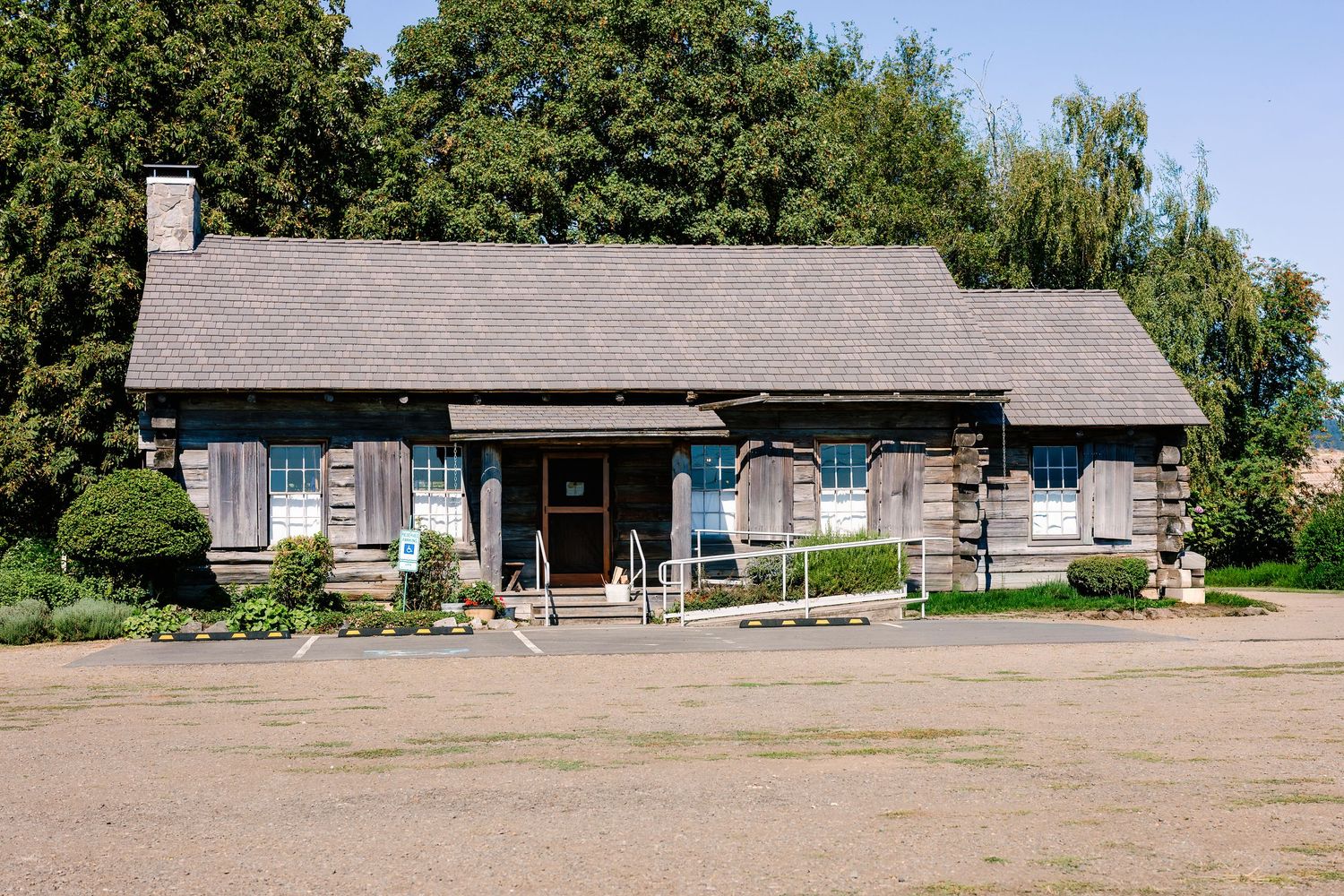 Row of rustic gray buildings with wooden trim against a tree-lined backdrop.