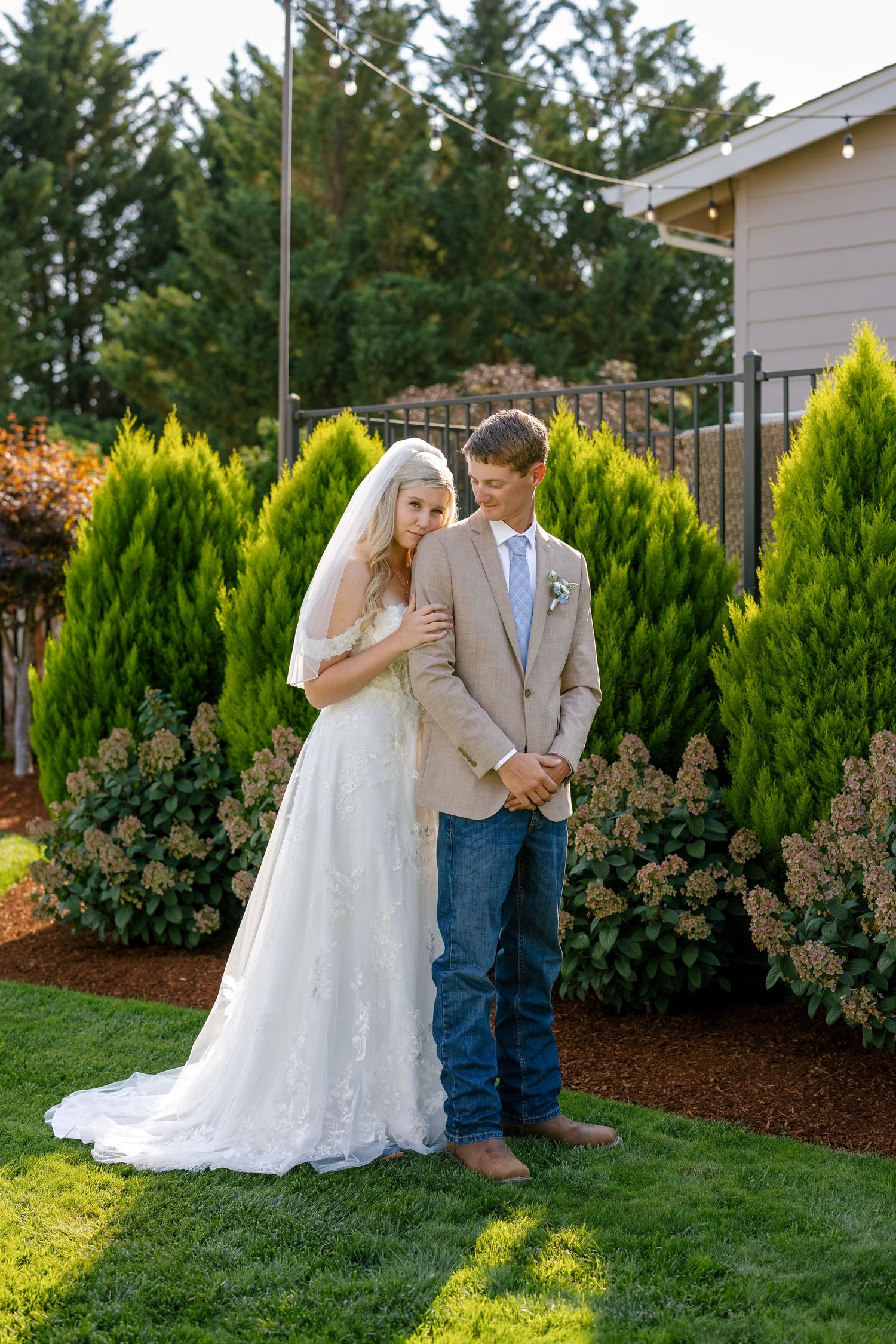 A couple shares intimate moments in a garden setting with evergreen trees and mulch landscaping.