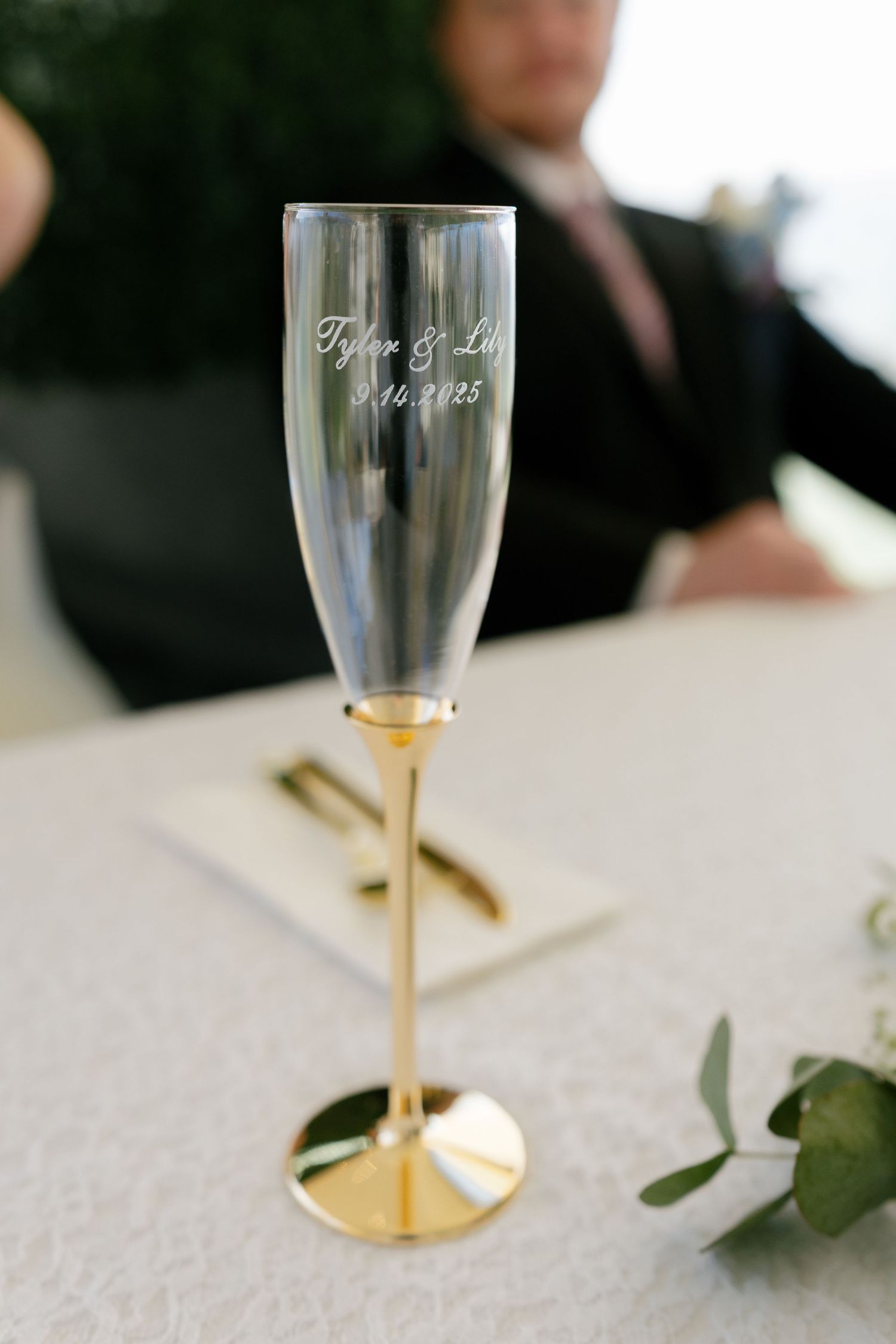 Elegant champagne glasses with gold stems sit on a white tablecloth at a wedding reception.