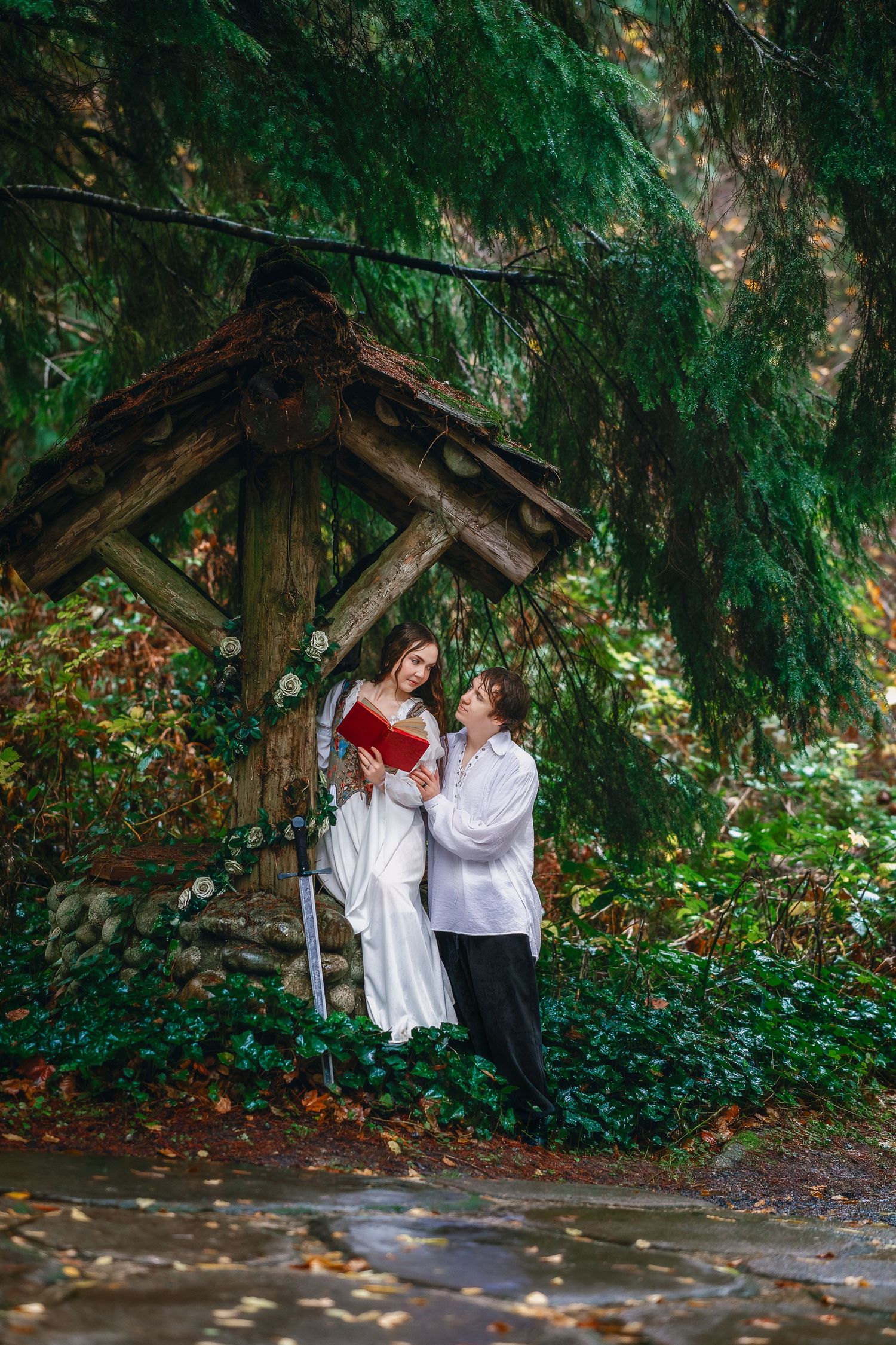 Two people in light clothing share a romantic moment under evergreen trees.