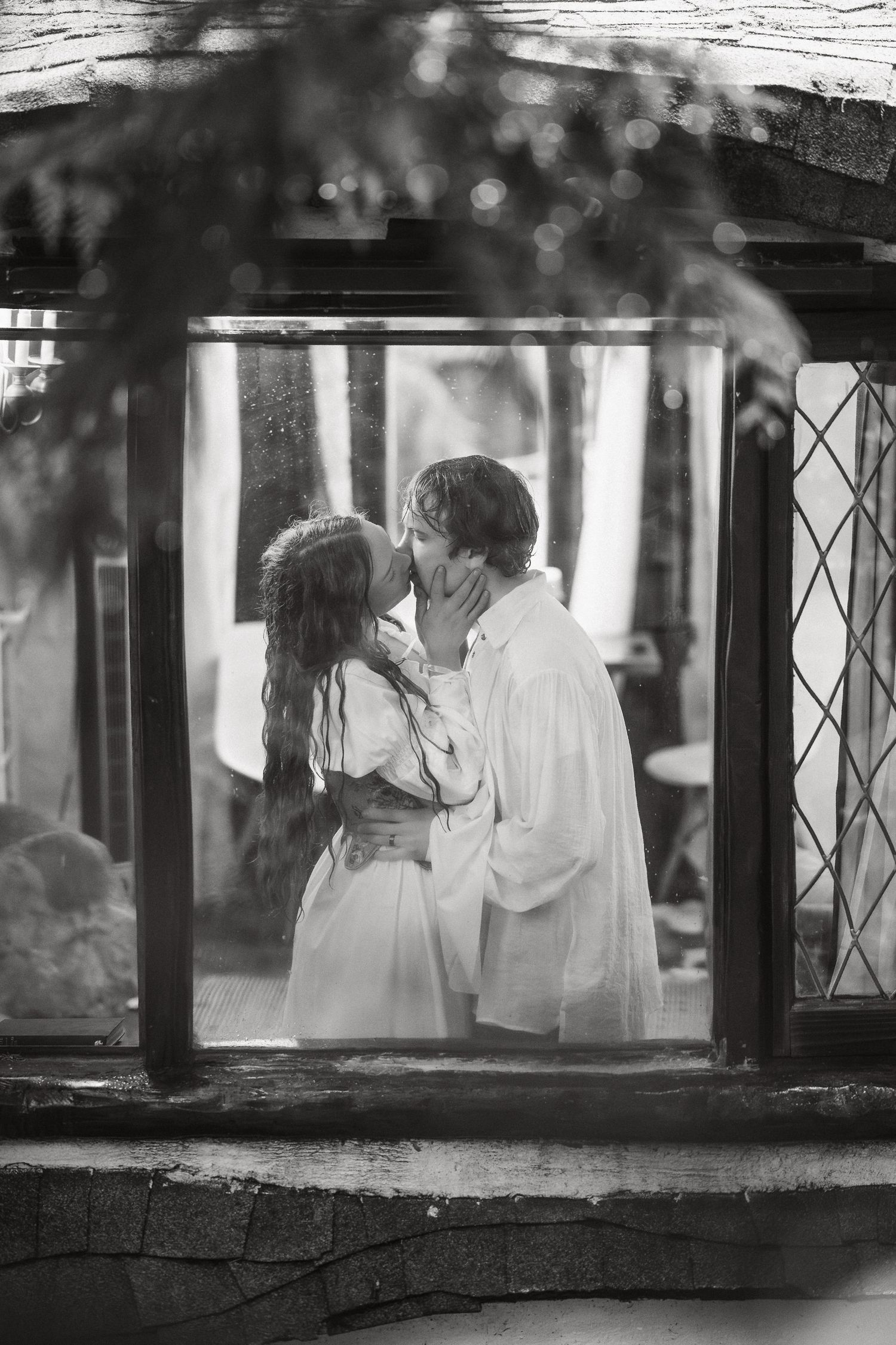 A black and white photo captures two silhouettes through a window frame.