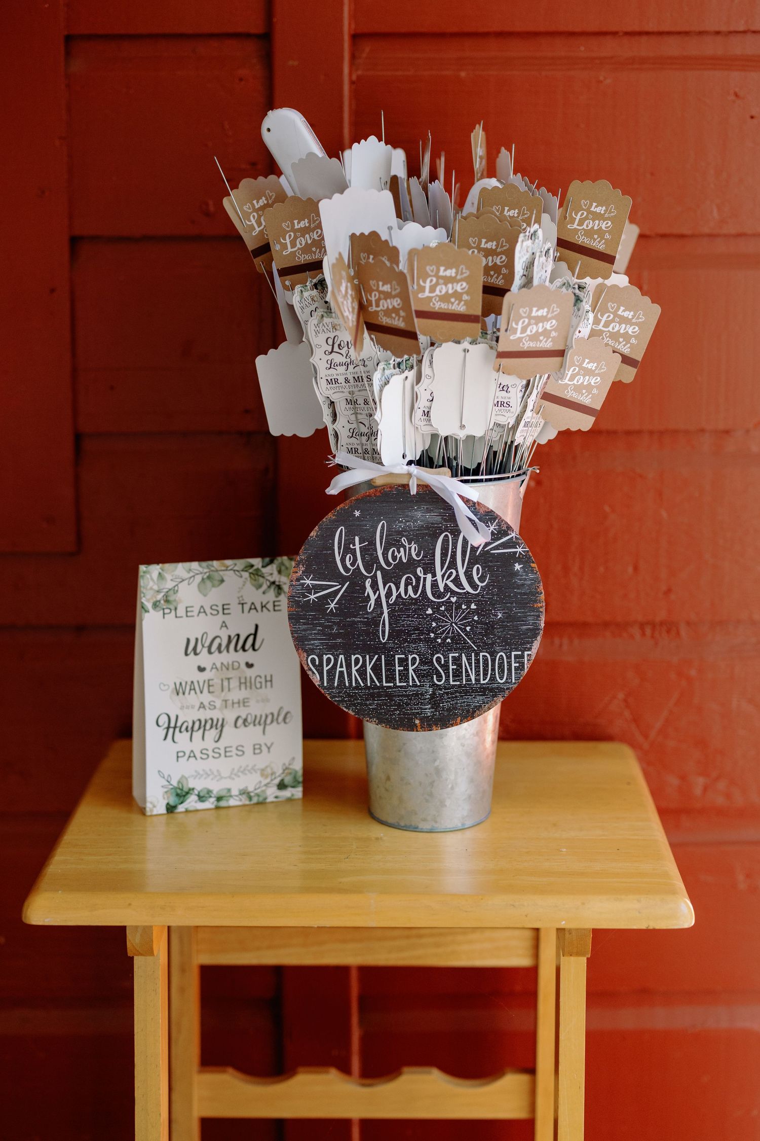 Wedding sparkler send-off signs displayed on a wooden table with decorative holders against a red wall.
