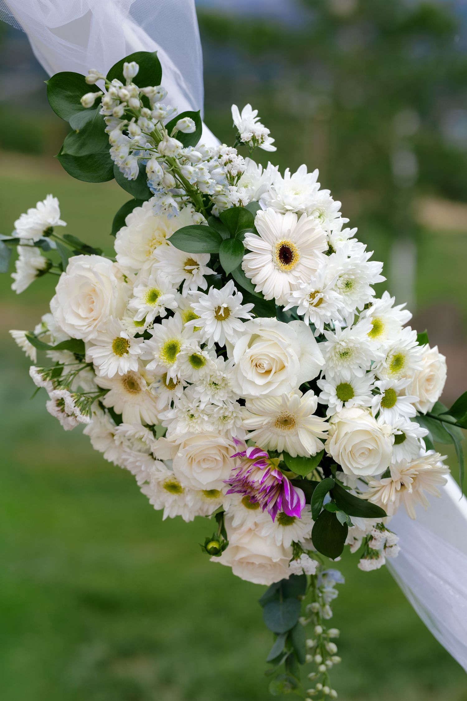 White roses and daisies create an elegant floral arch decoration against a green outdoor backdrop.