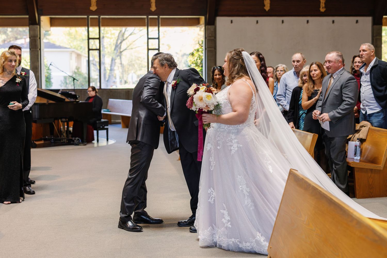 Wedding guests seated in rows at an indoor ceremony venue with natural light streaming through windows.