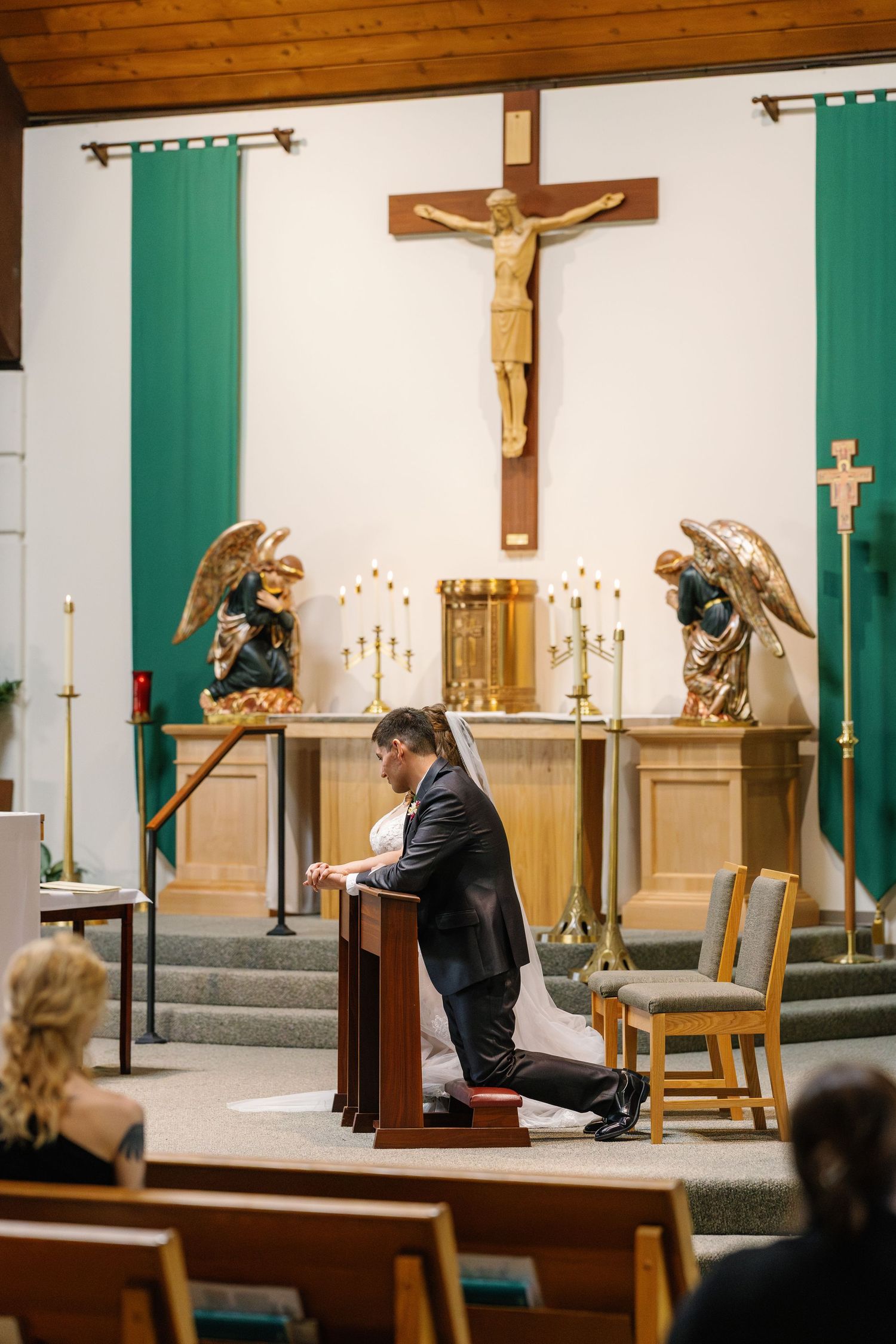 A church altar with crucifix, green banners, and golden angels during a religious ceremony.