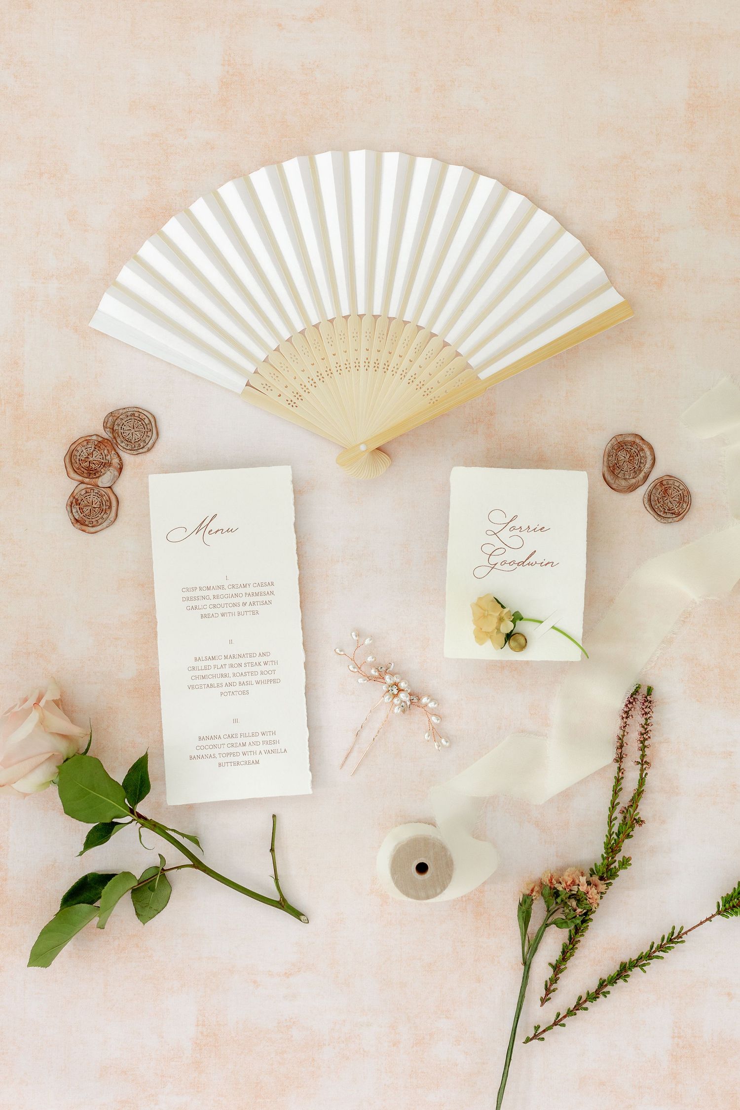 Elegant wedding stationery flatlay with white paper fan, floral elements, and delicate pink accents.