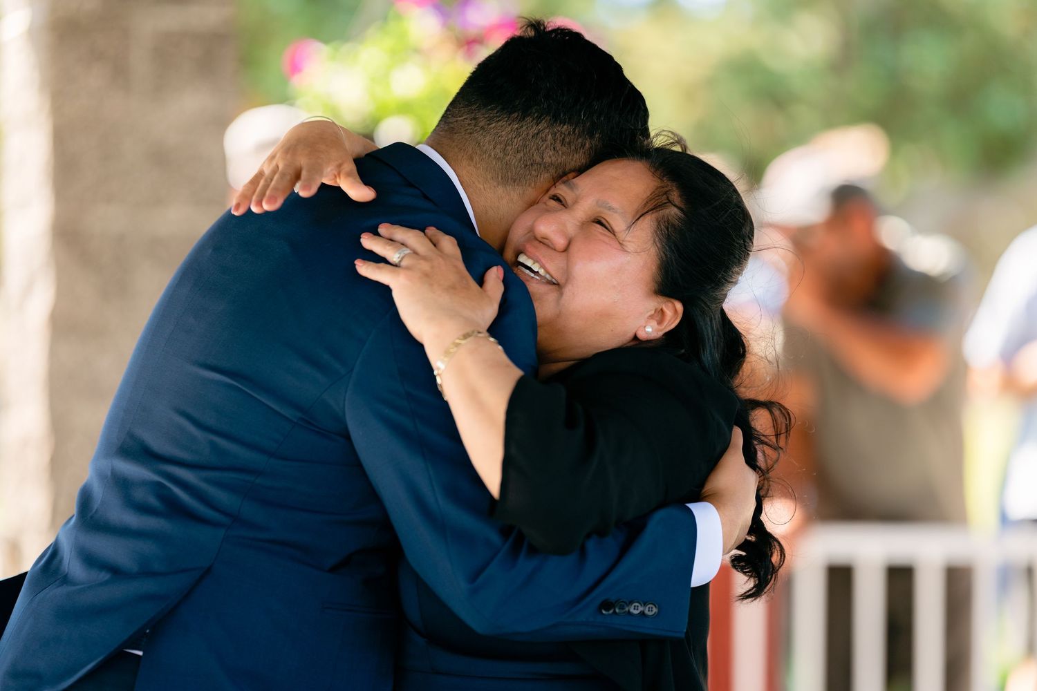 Emotional mother hugs her son in a navy suit during a heartfelt wedding day embrace outdoors.