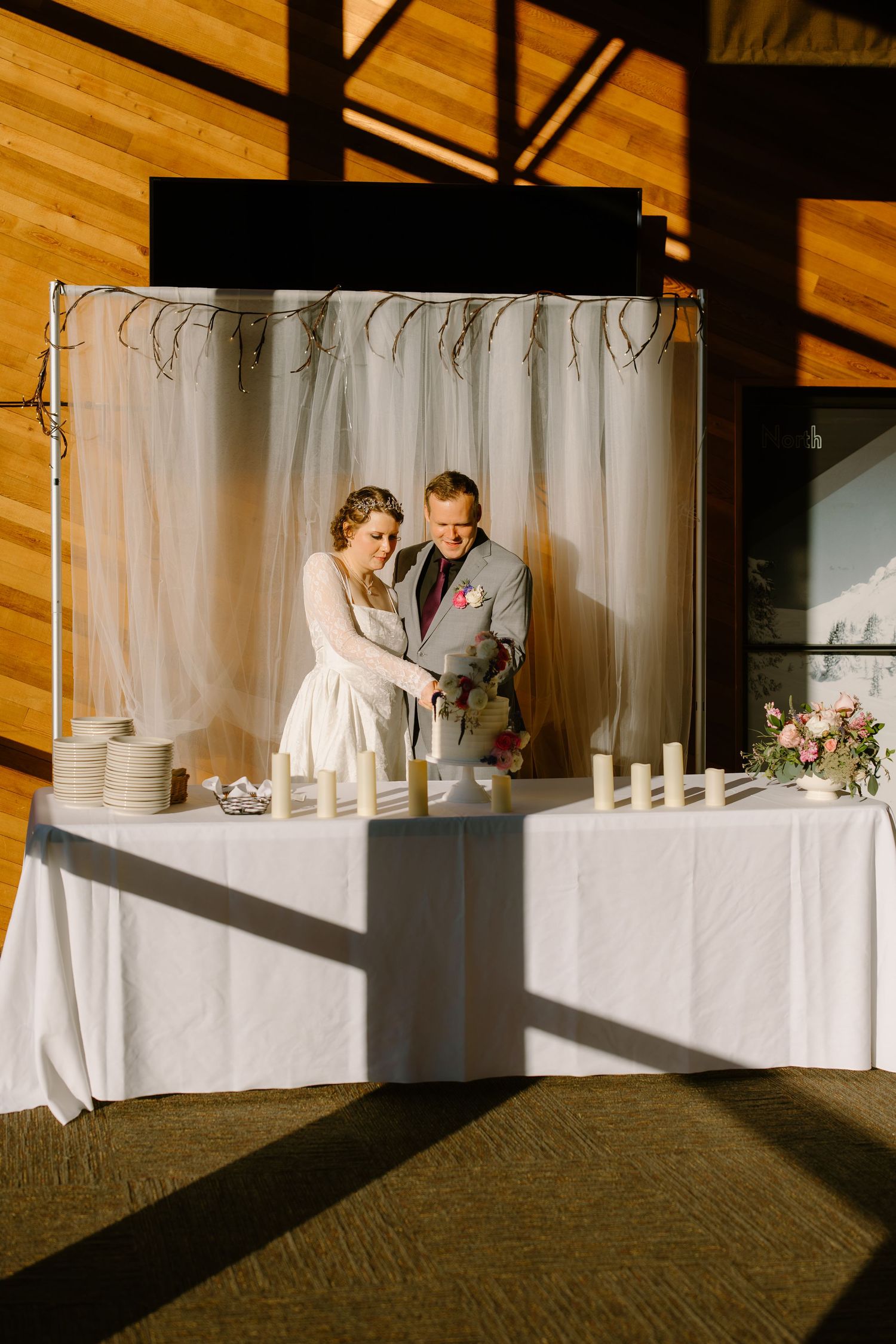 Bride and groom cutting their wedding cake at a decorated table with candles and sheer white backdrop.