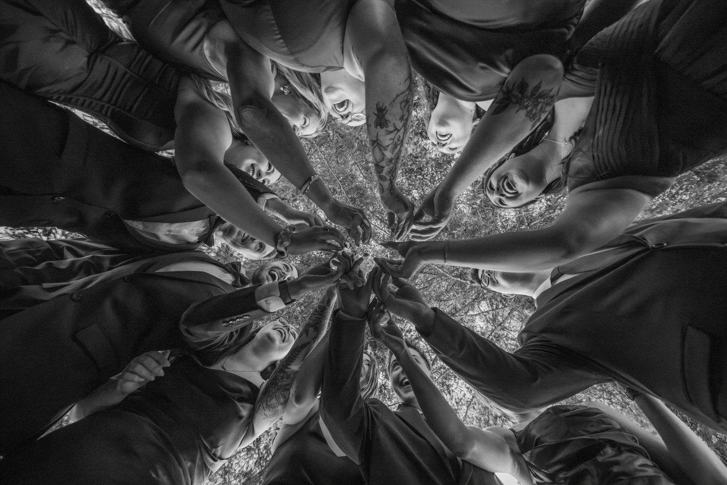 Black and white aerial view of wedding party forming a circle with hands joined in center.