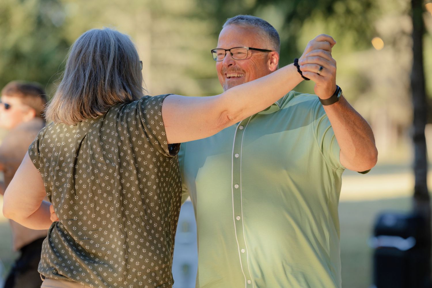 A smiling couple dances together outdoors at a sunny wedding reception celebration.