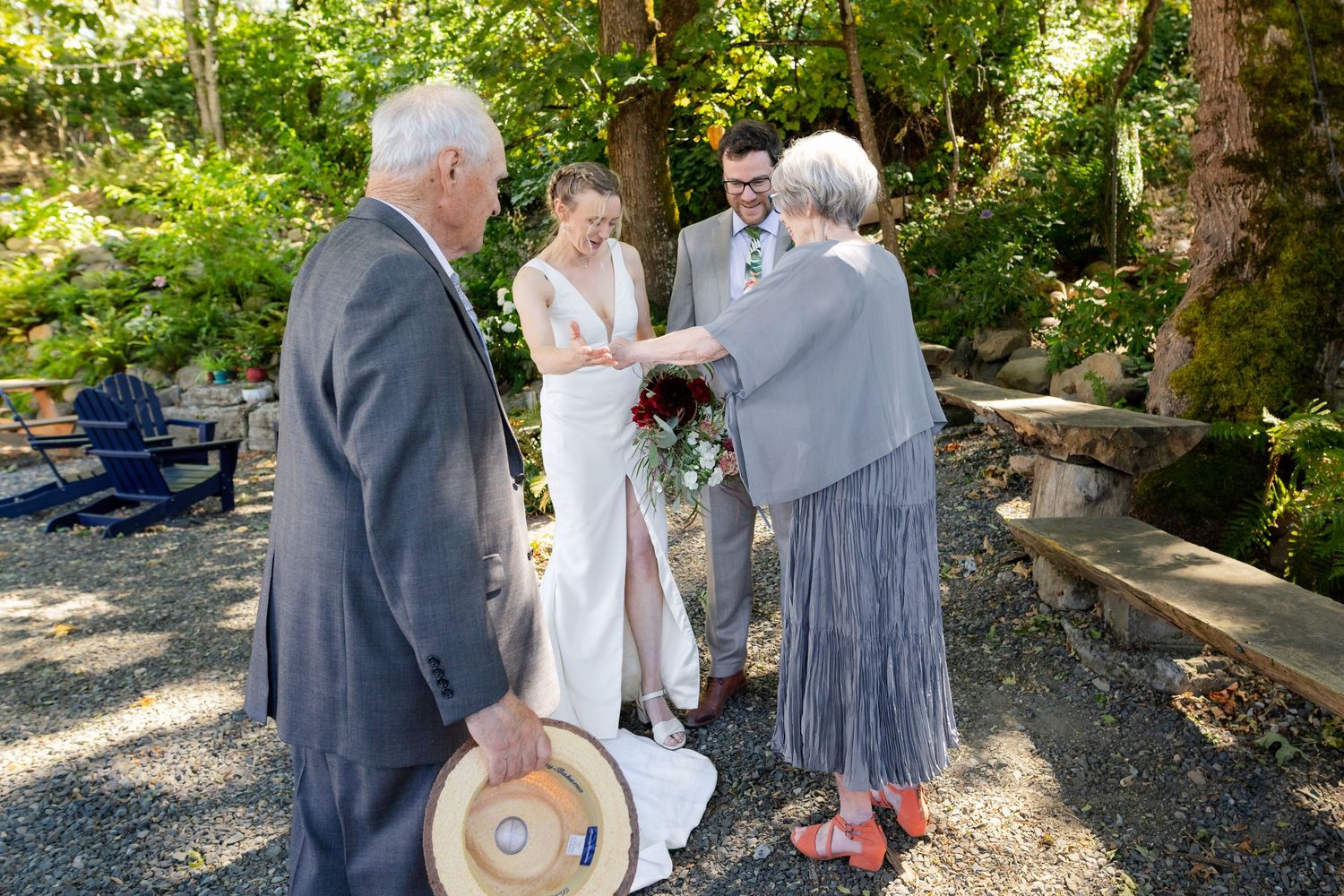 Outdoor wedding ceremony with bride and groom exchanging vows with elderly guests in a lush garden setting.