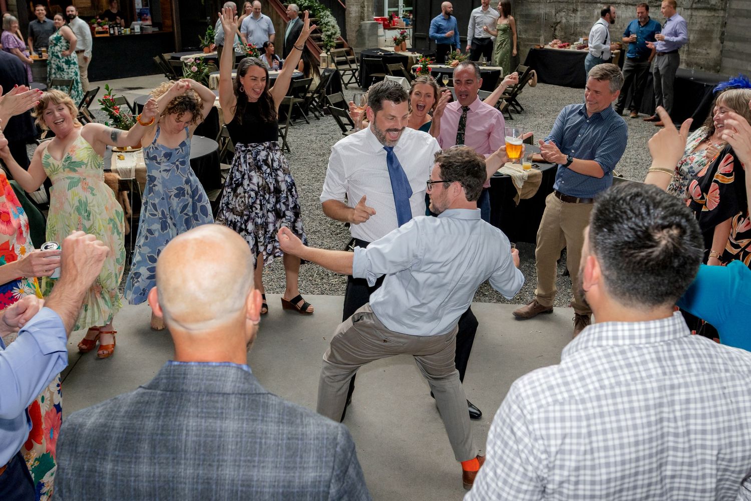 Wedding guests energetically dancing in a circle outdoors at a lively wedding reception celebration.