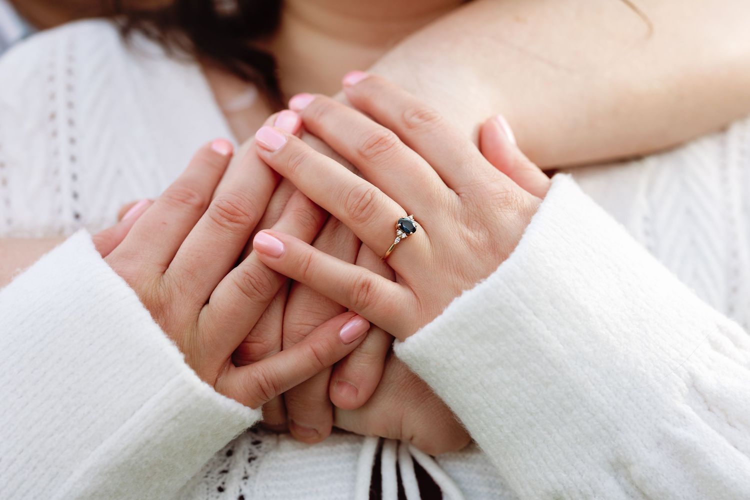 Close-up shot of hands tenderly clasped together showing an engagement ring.