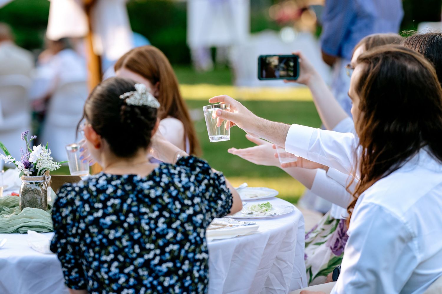 Wedding guests clink clear plastic cups in toast at outdoor evening reception.