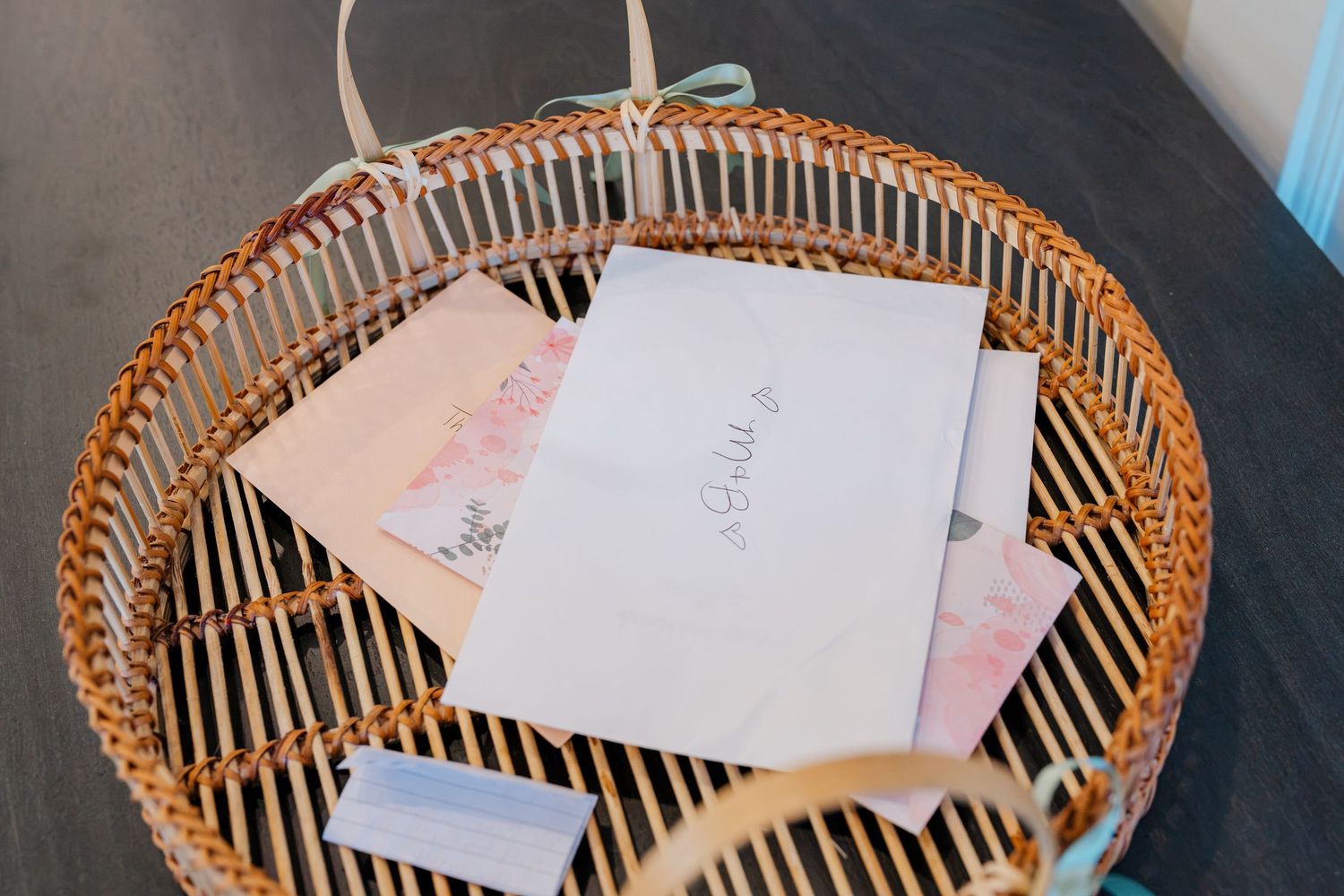 Wicker basket holding wedding cards and envelopes on a dark wooden table.