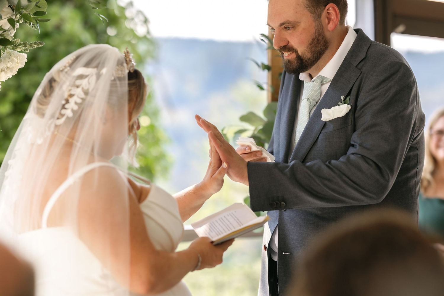 A couple exchanges vows during an outdoor wedding ceremony with the bride in white veil and groom in dark suit.