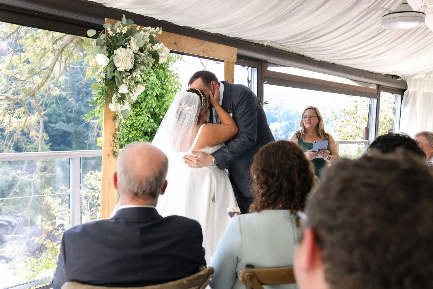 Elegant wedding reception under a white tent with floral arrangements and guests seated at tables.