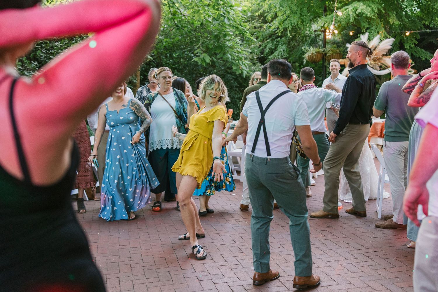 Wedding guests dance together on an outdoor brick patio during a summer celebration.