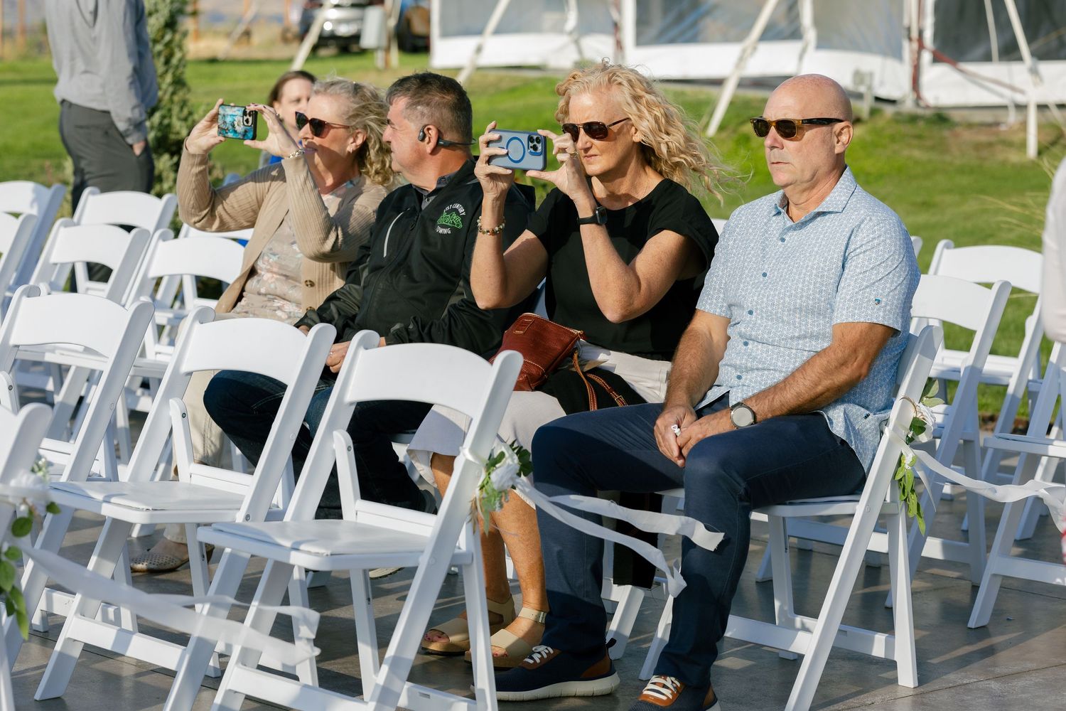 White folding chairs are set up for an outdoor wedding ceremony on a sunny day.