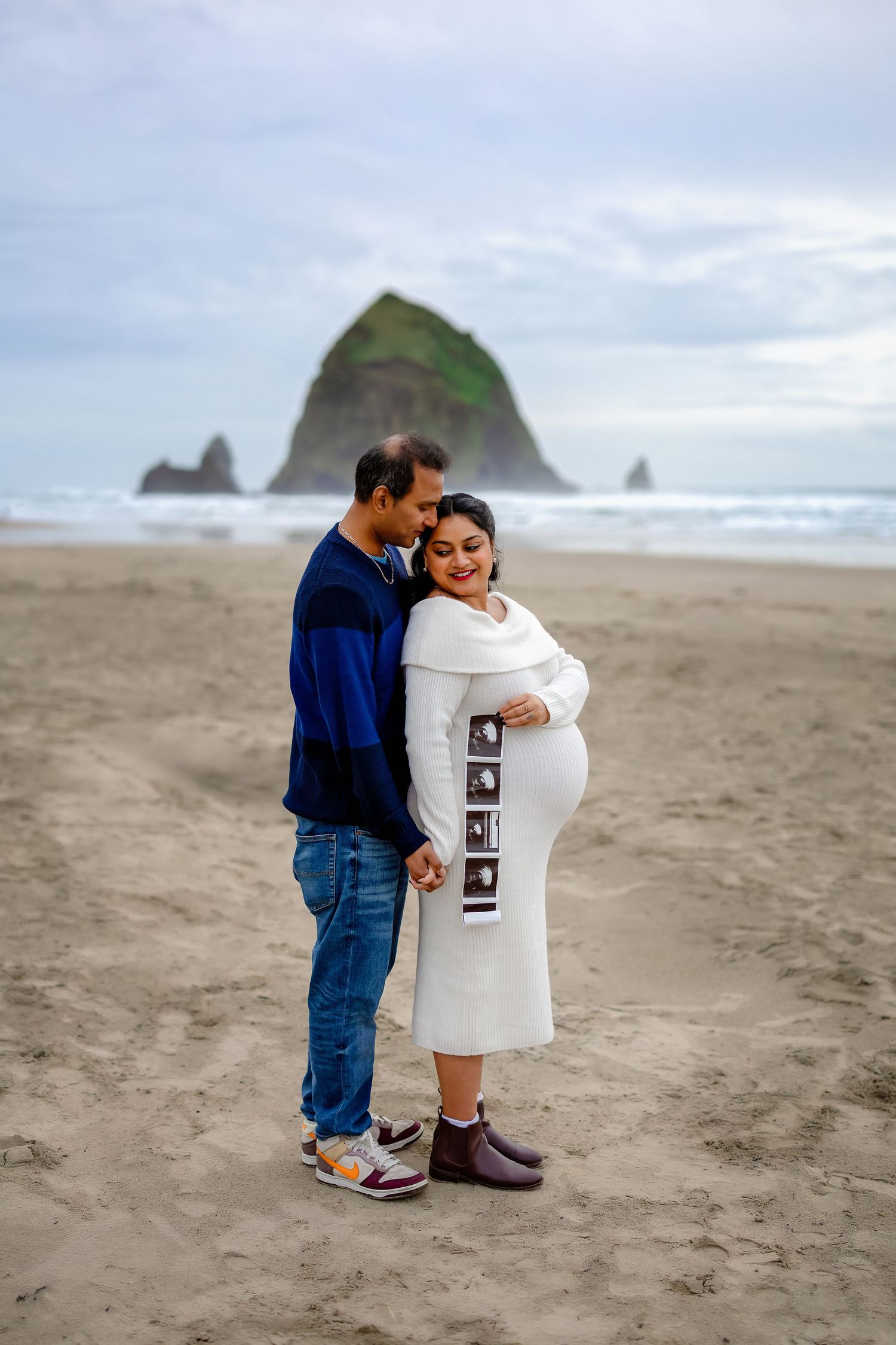 A couple shares an intimate moment on Cannon Beach with iconic Haystack Rock in the background.