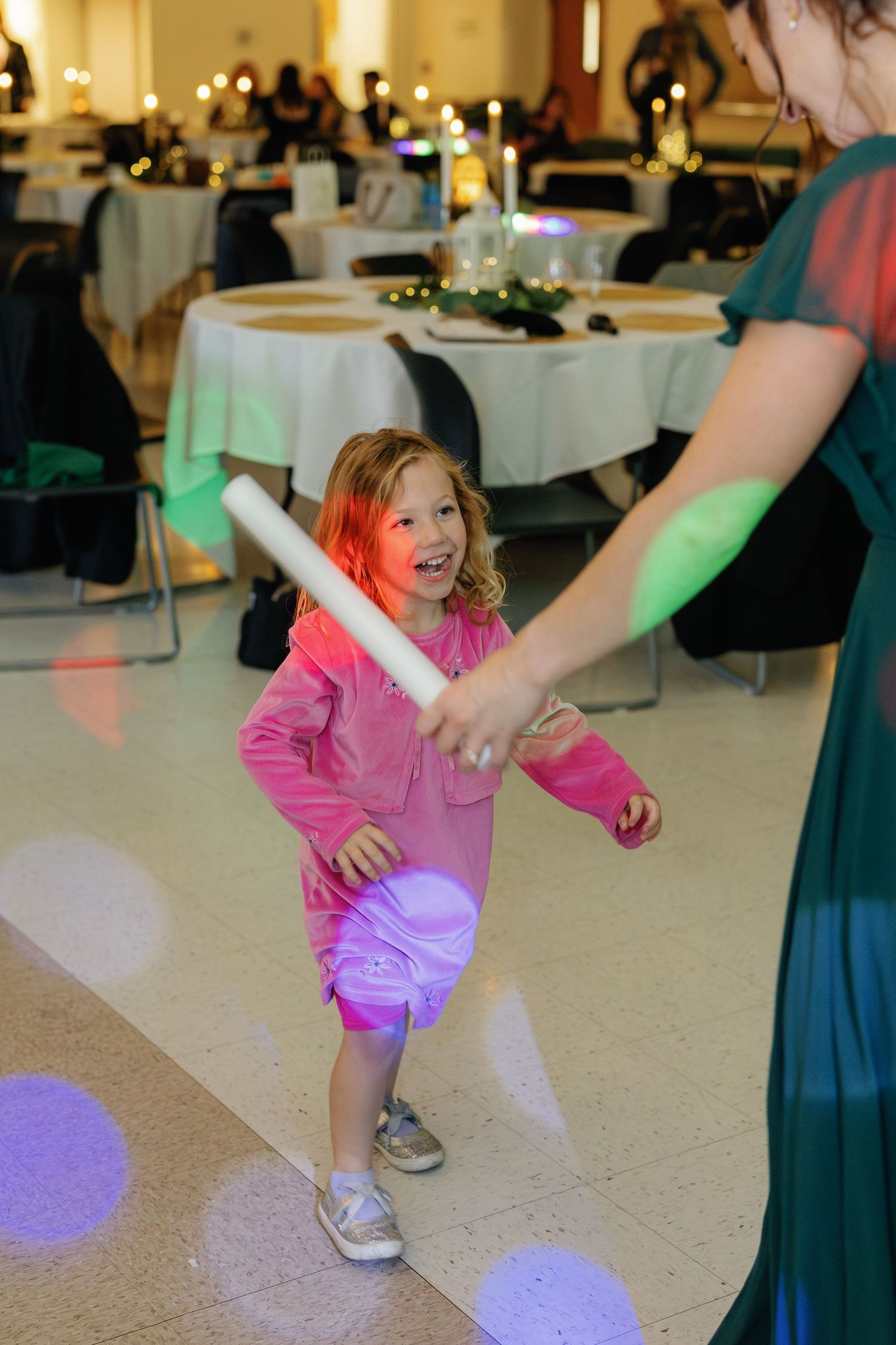 Young dancer in pink performs energetic moves on the reception dance floor under colorful lights.