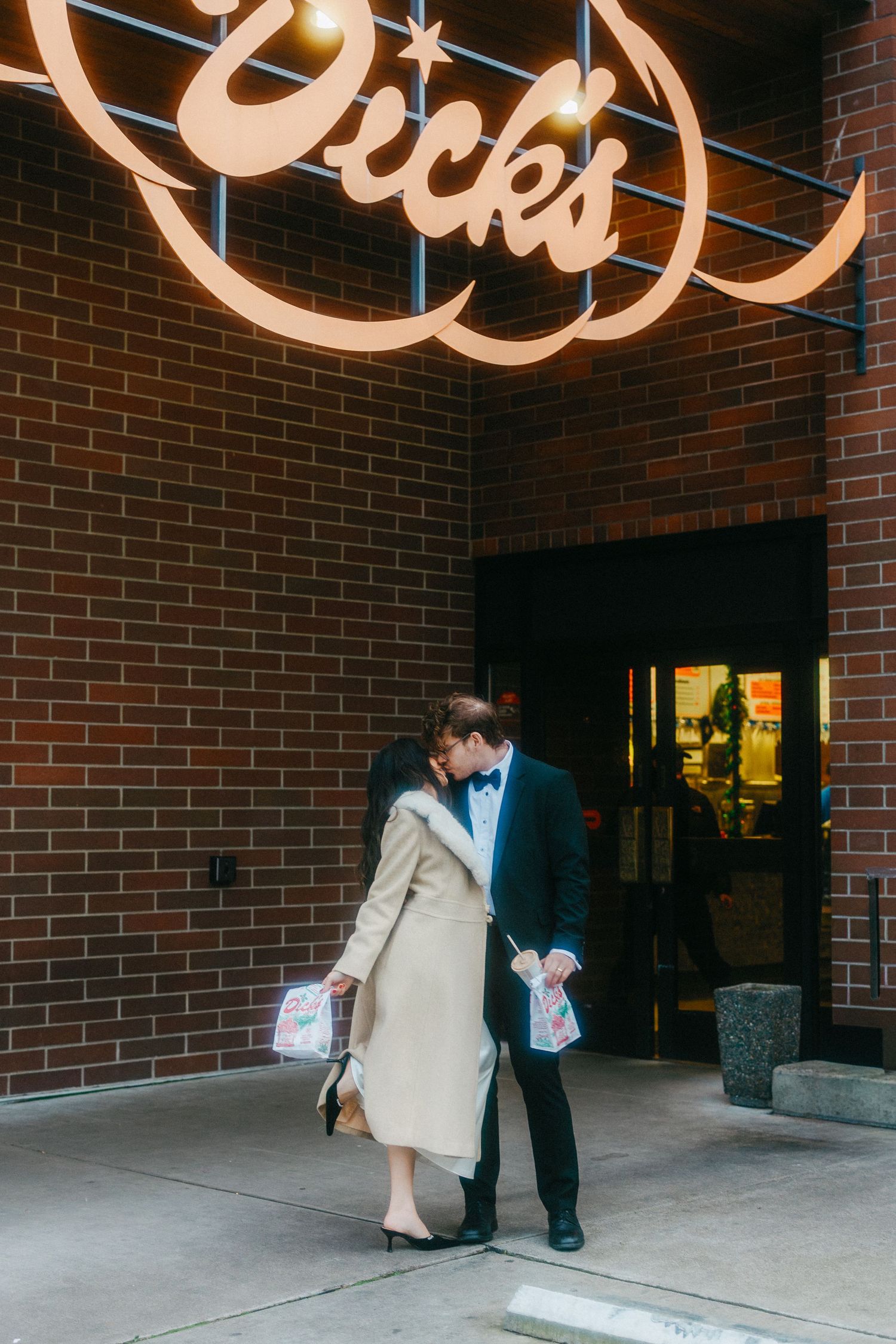 A couple stands beneath illuminated signage outside a brick building entrance.