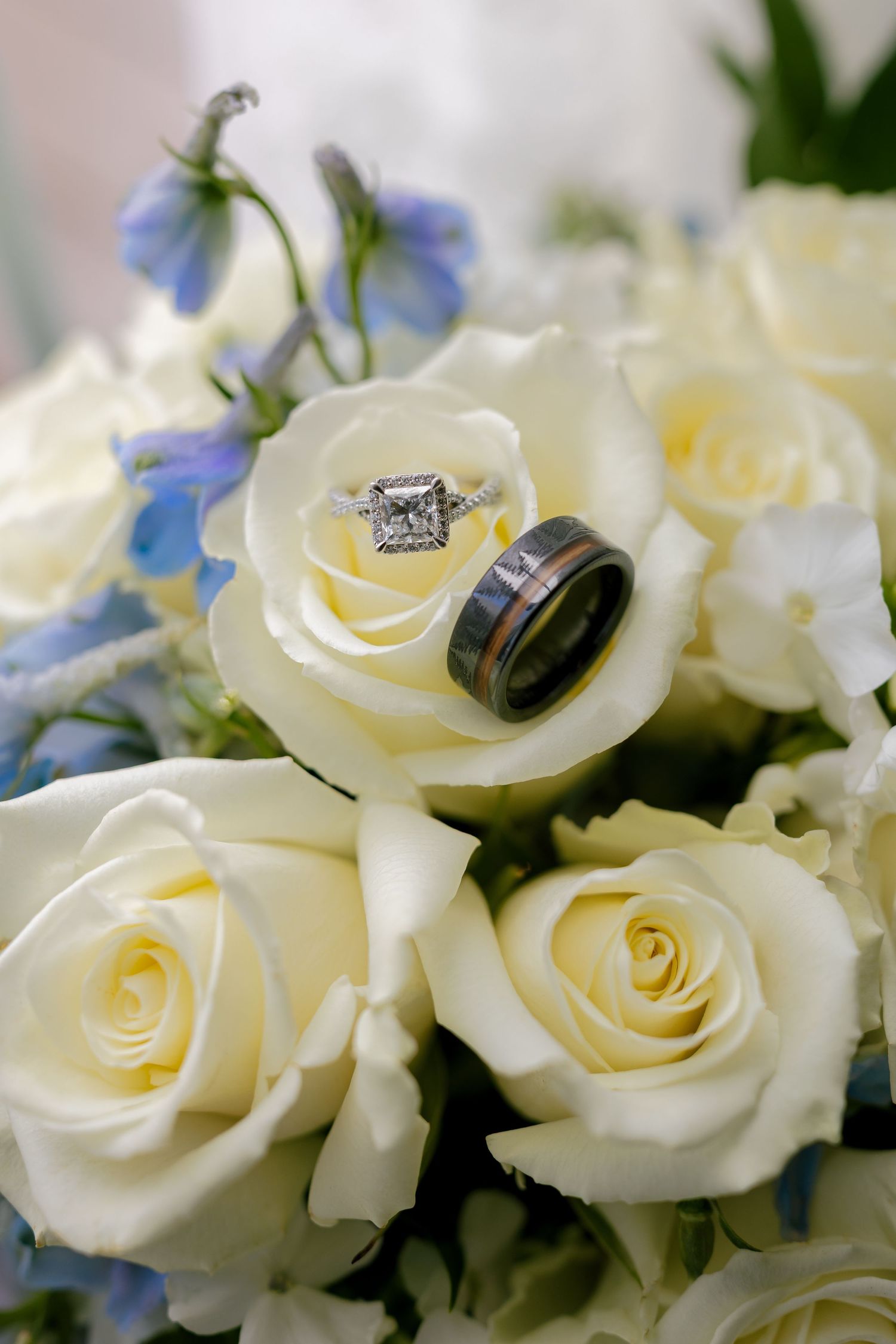 Wedding rings nestled in delicate white roses with soft blue flowers in the background.