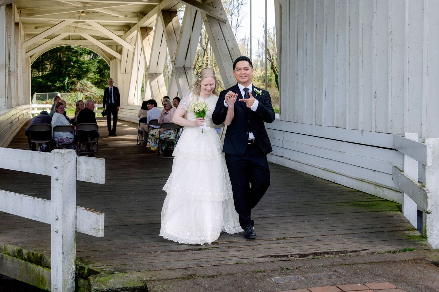 Bride and groom walk joyfully through a covered wooden bridge after their wedding ceremony.