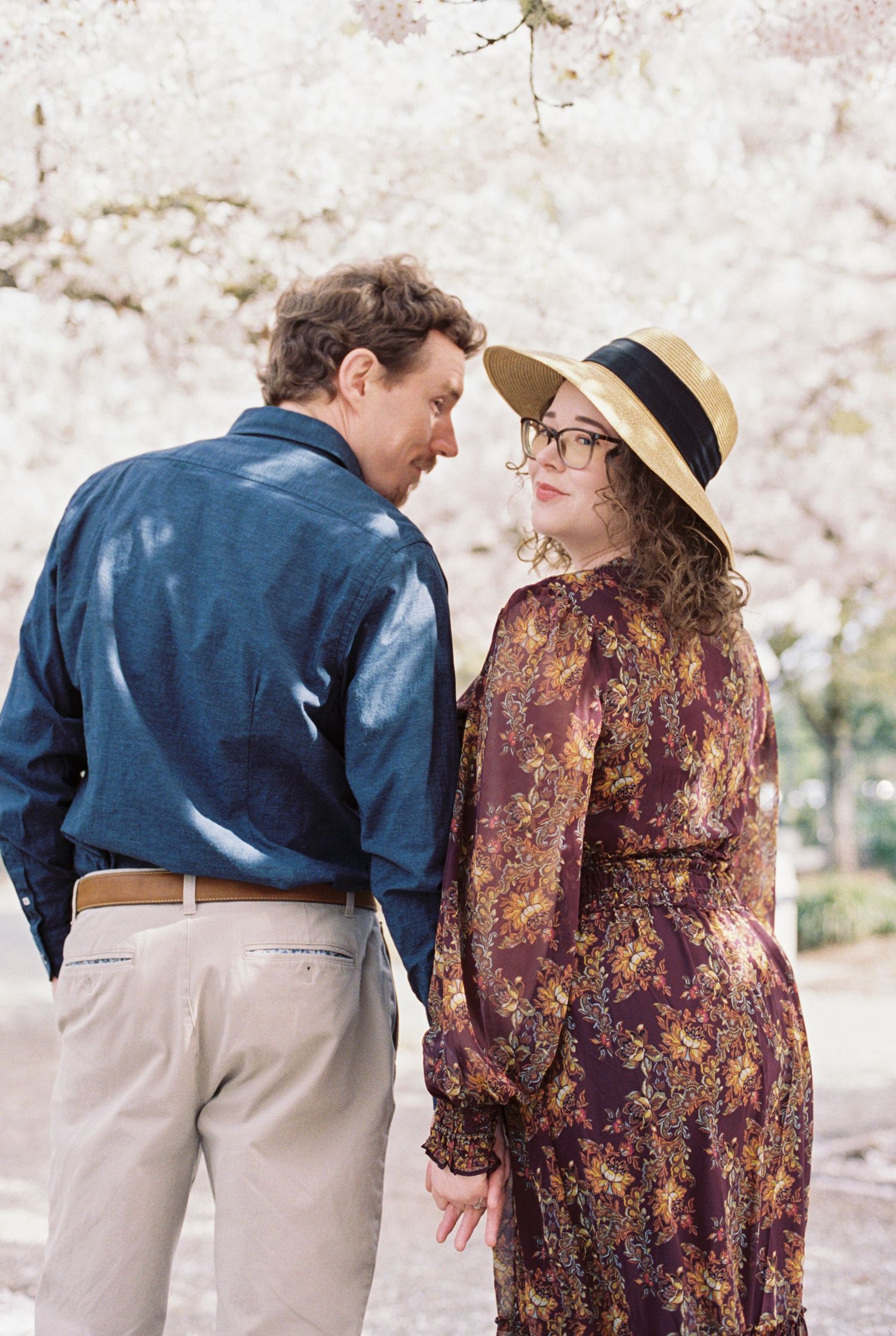 A couple in coordinating blue and floral outfits share a romantic moment while walking outdoors during spring.