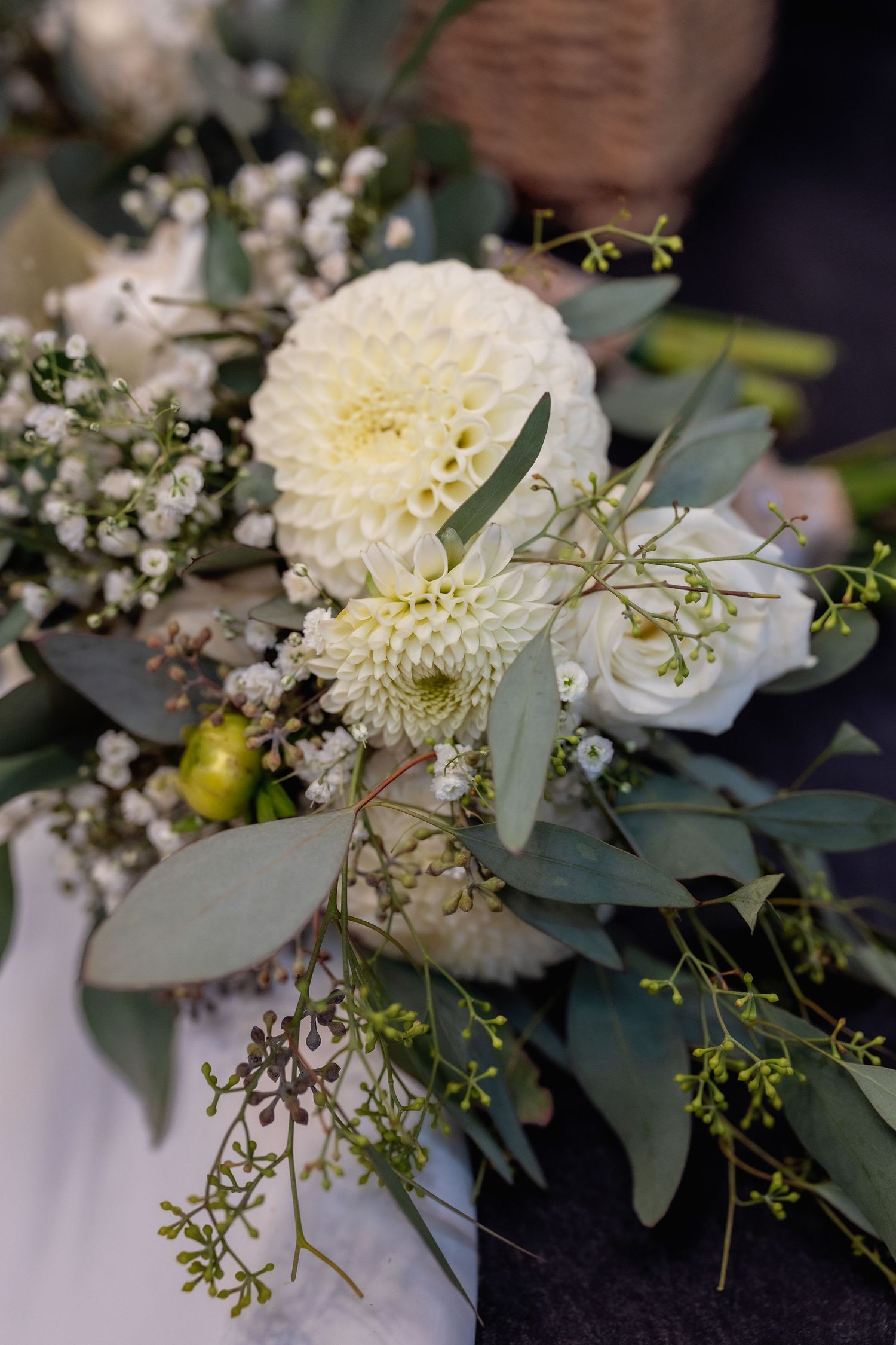 Delicate white floral arrangement with eucalyptus leaves and baby's breath on dark background.